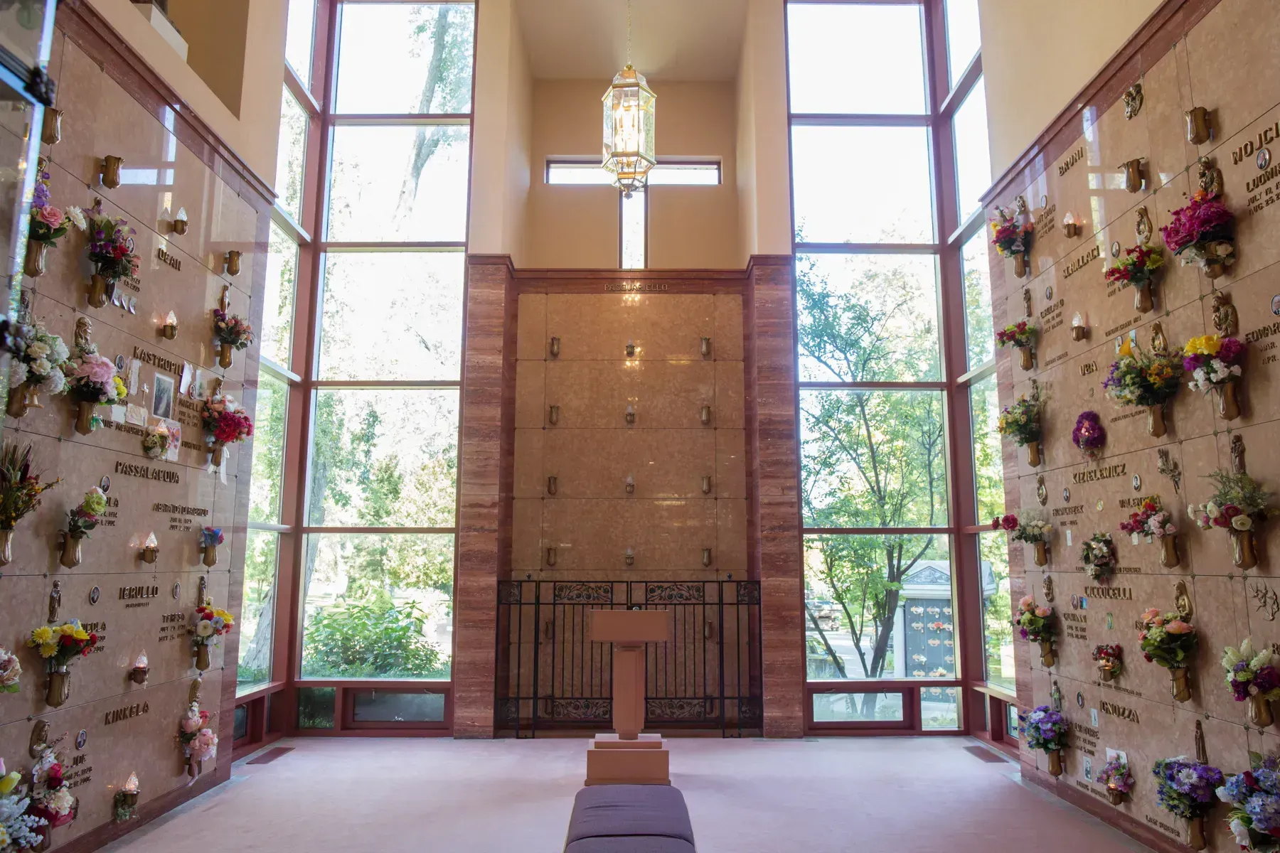 Indoor chapel with tall windows, flower-lined walls, and a central altar against a wooden backdrop