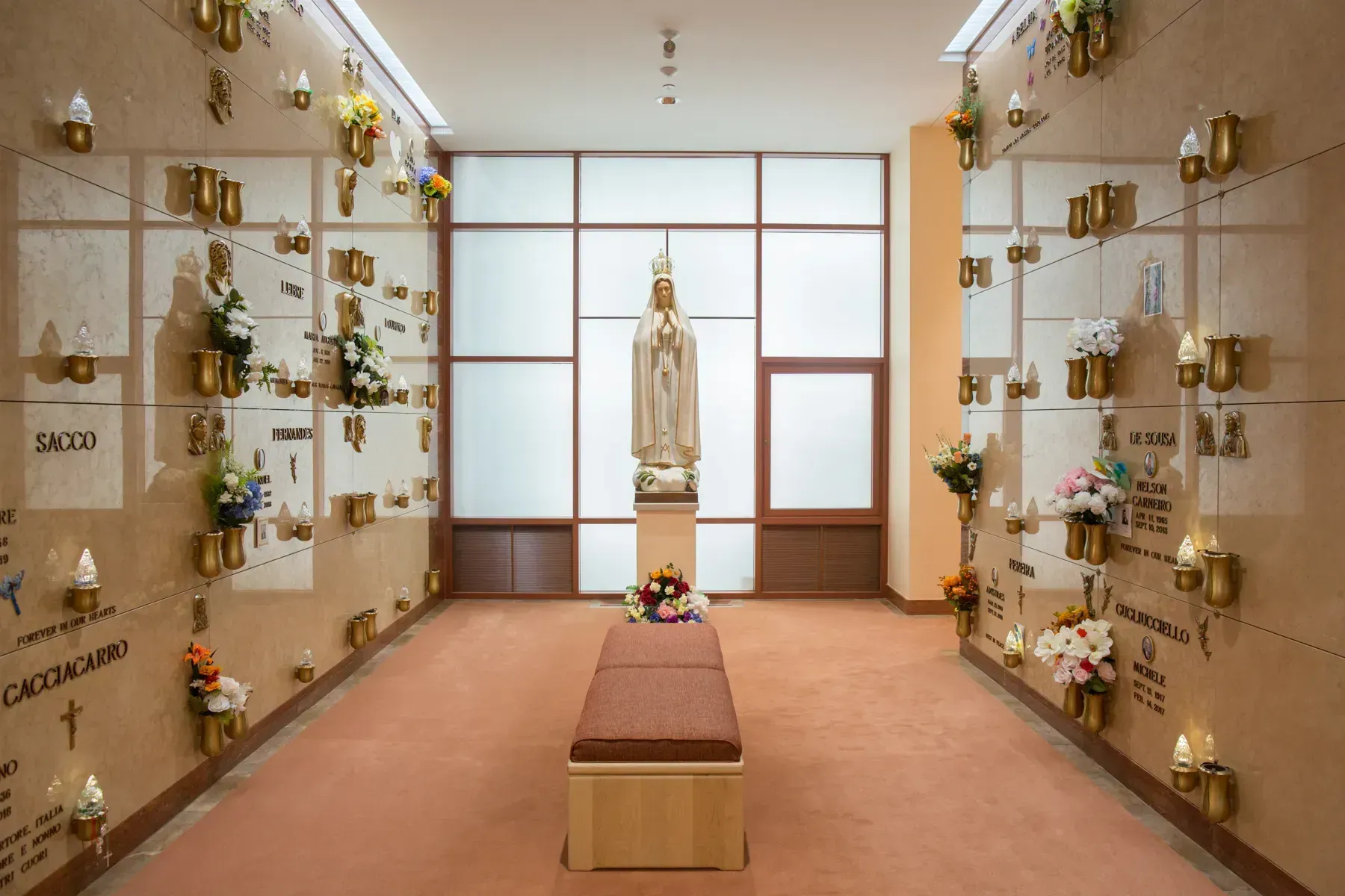 A quiet chapel with a central statue, floral arrangements, and rows of memorial niches on both sides.