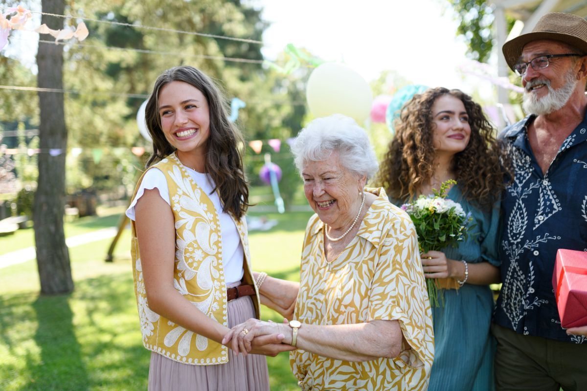 Four people smiling and shaking hands at an outdoor gathering in a sunny park