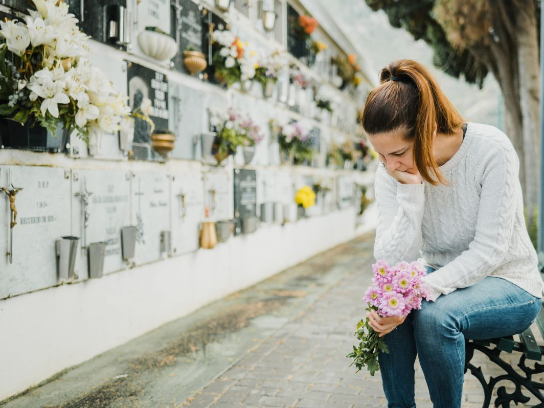 Woman kneeling at a cemetery wall, placing pink flowers among white memorial bouquets