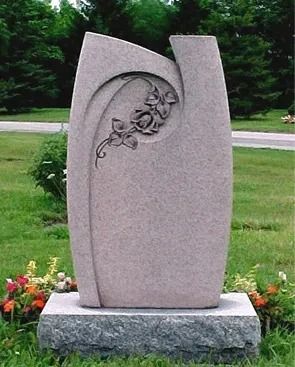 Gray abstract stone memorial with floral carving on a pedestal in a grassy outdoor setting