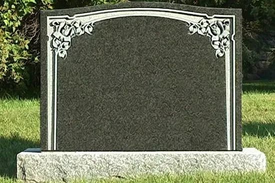 Empty granite gravestone with ornate white floral corners in a grassy cemetery.