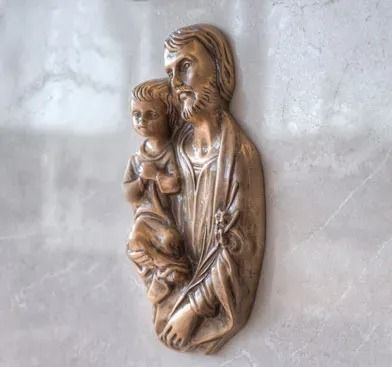 Relief sculpture of a bearded man holding a child on a pale stone wall