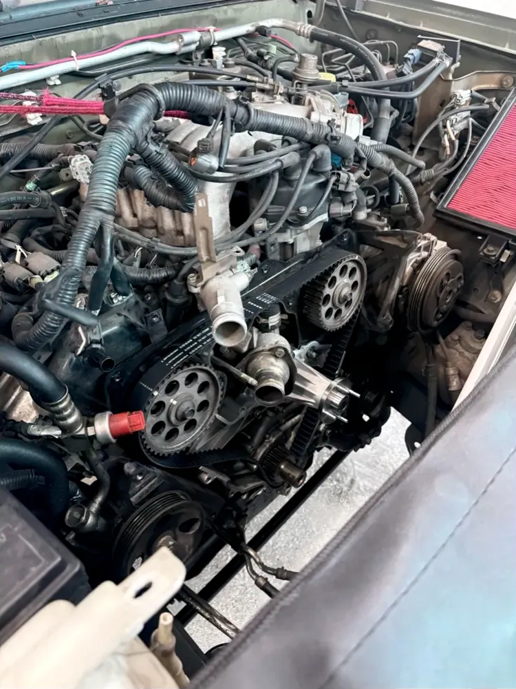 Car engine with exposed belts and components, viewed from above, likely under repair. | Supreme Auto Repair Shop