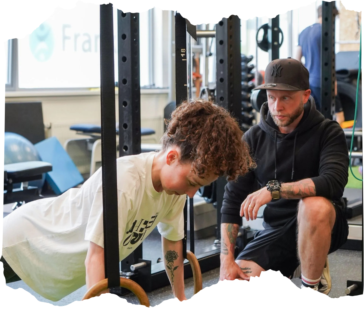 Een trainer begeleidt iemand bij het doen van push-ups in een sportschool, omringd door fitnessapparatuur.