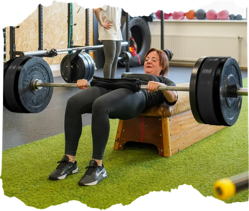Vrouw voert heupstoten uit met een halter in een sportschool, liggend op een bankje op kunstgras.
