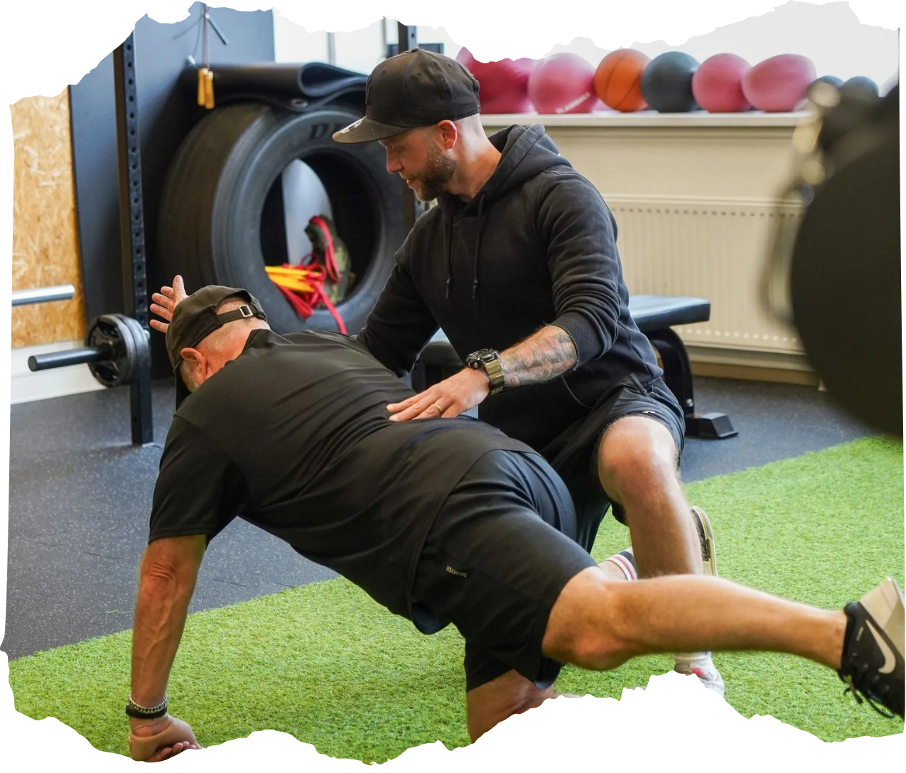 Een trainer helpt iemand met een core-oefening op kunstgras in een sportschool.
