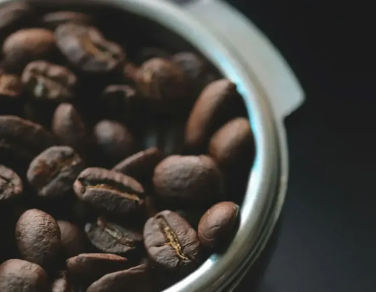 Close-up of roasted coffee beans in a metal bowl on a dark background