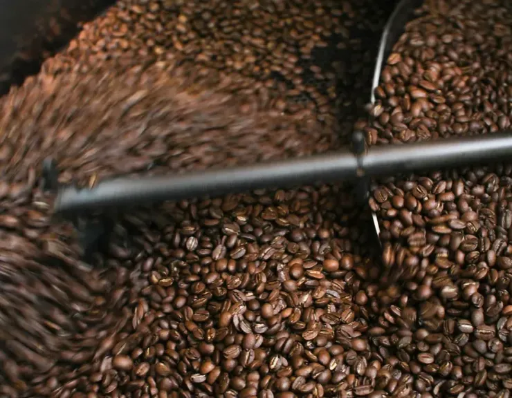 Coffee beans tumbling in a roasting drum with a metal rod crossing the frame