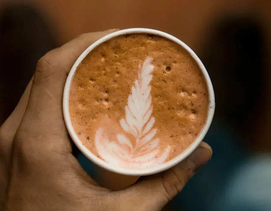 Hand holding a cup of coffee with latte art on top