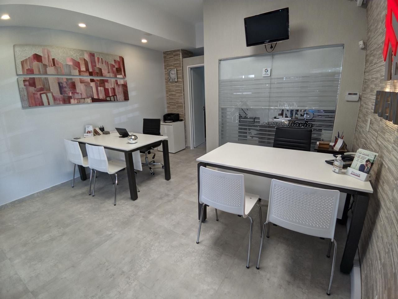 Oficina o sala de reuniones moderna con escritorios blancos, sillas, obras de arte en las paredes y un televisor montado detrás de mamparas de vidrio.