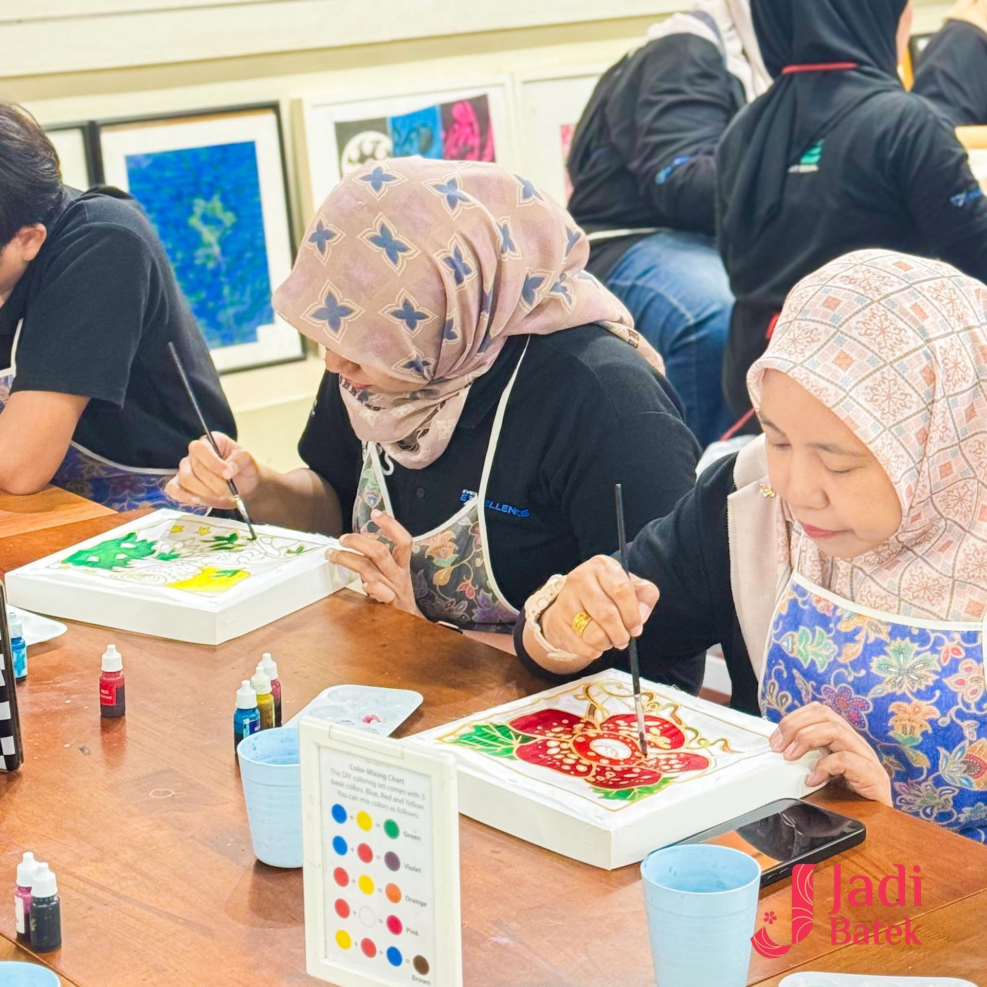 People at a batik painting workshop, seated around a table, painting designs with brushes and colorful dyes.