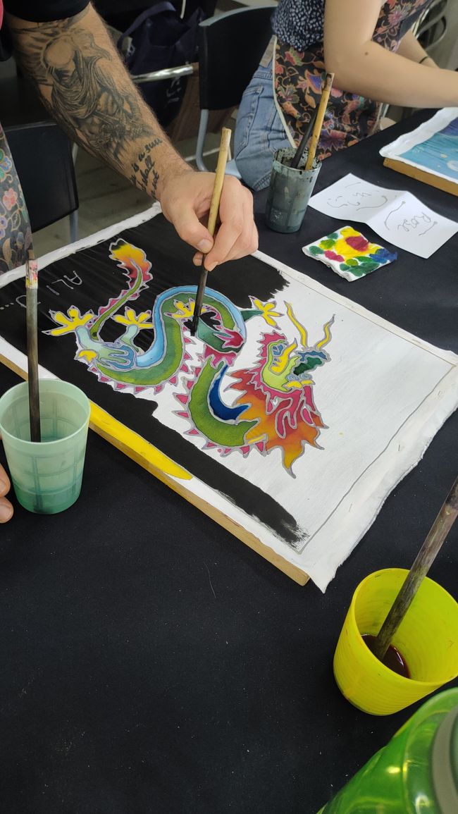 Person painting a colorful dragon with brush on fabric at a table.