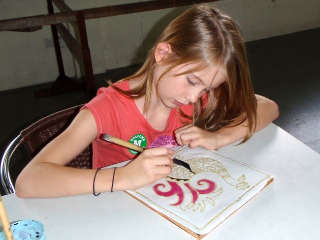 Girl painting a design with a brush on a white surface, indoors.