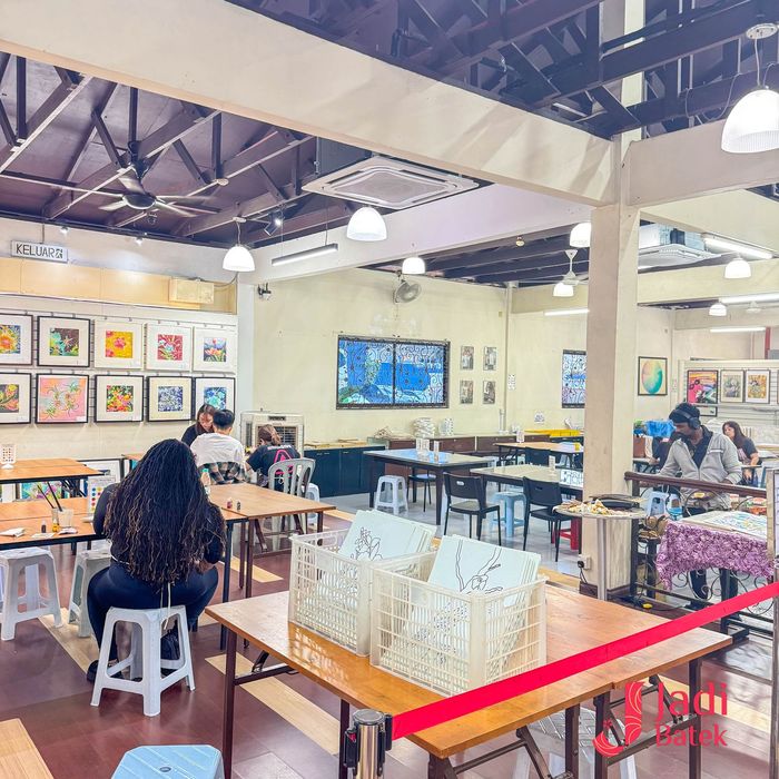 Art studio with tables, paintings, and people creating. Bright, airy space.