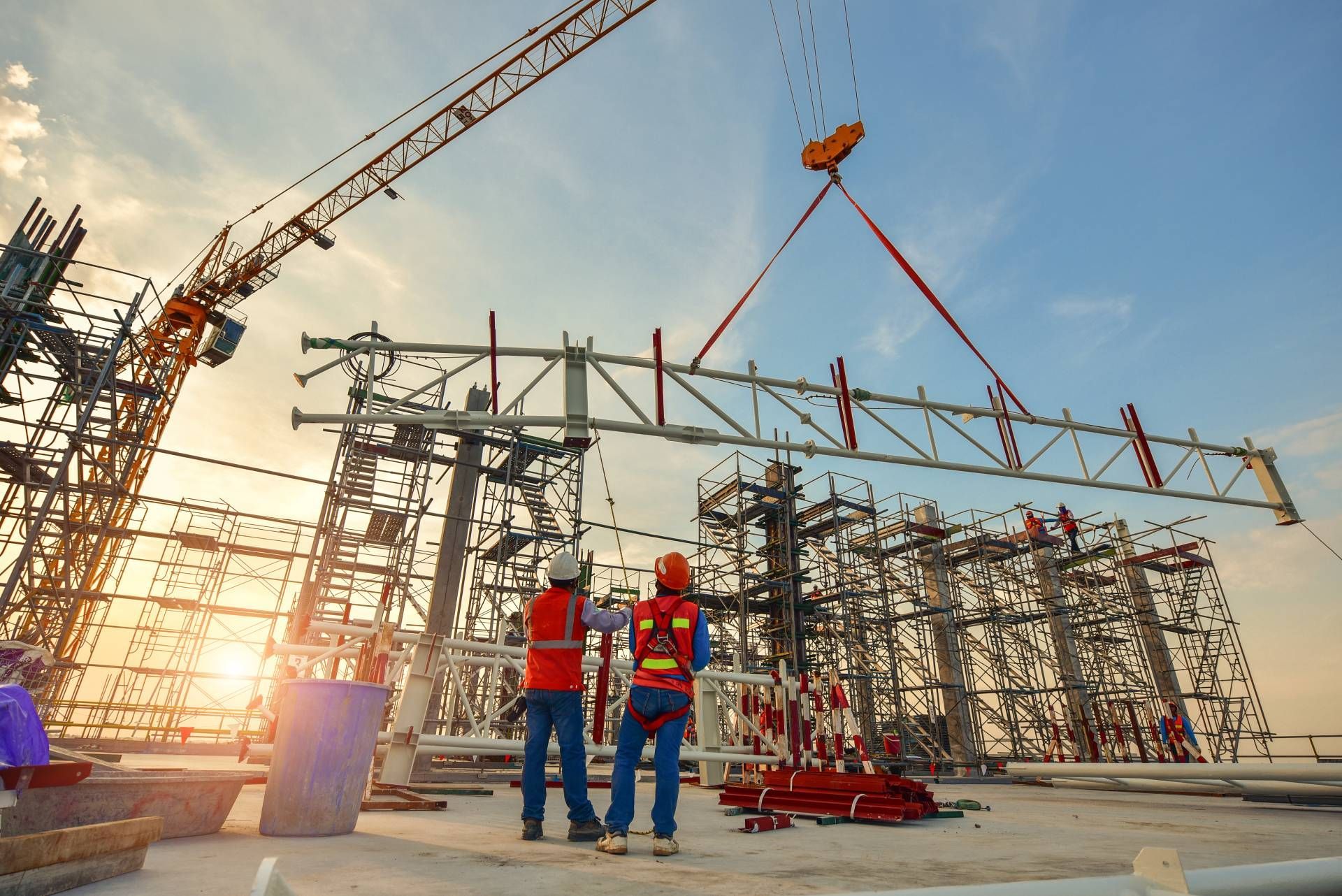 Two construction workers are standing in front of a crane at a construction site.