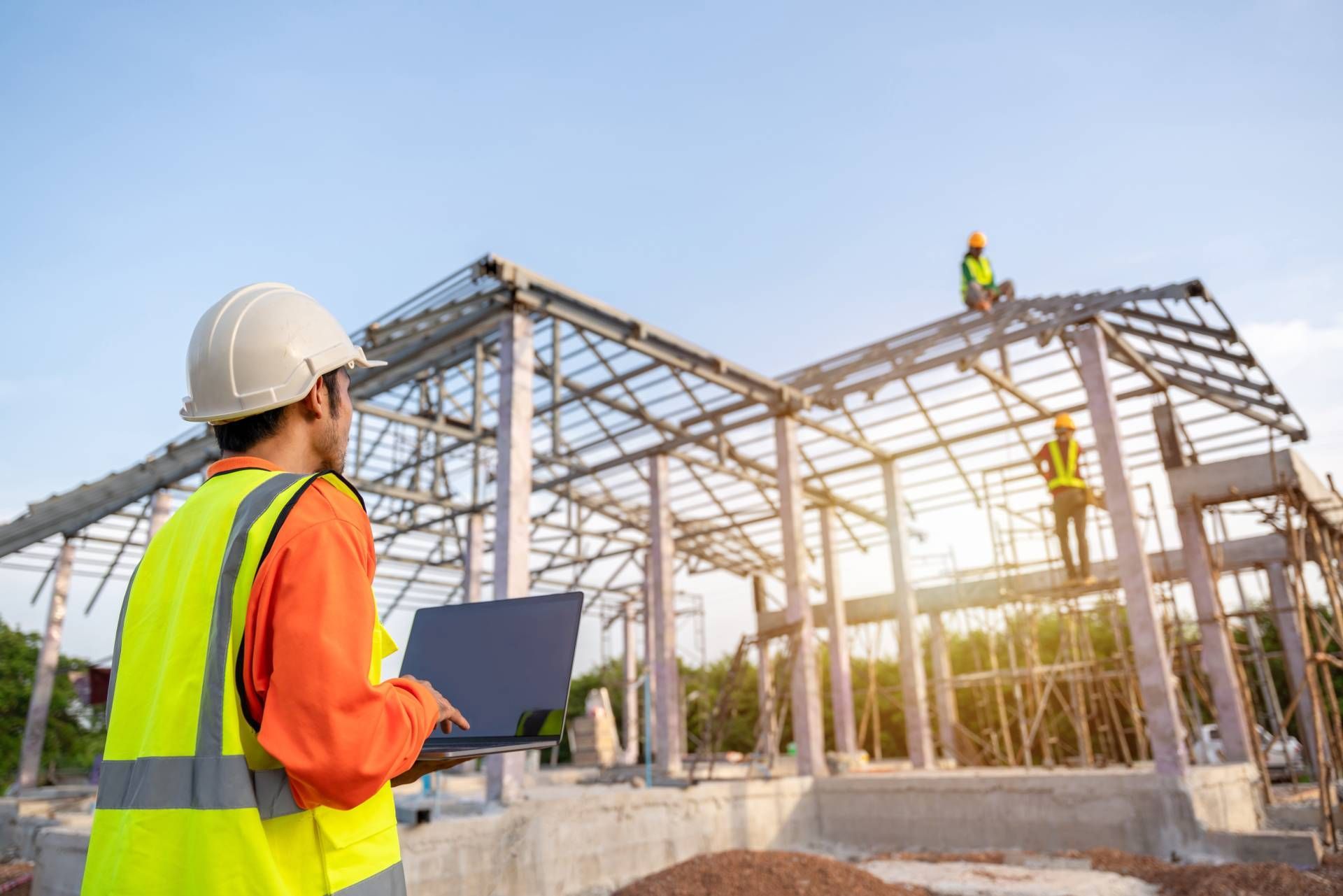 A construction worker is holding a laptop at a construction site.