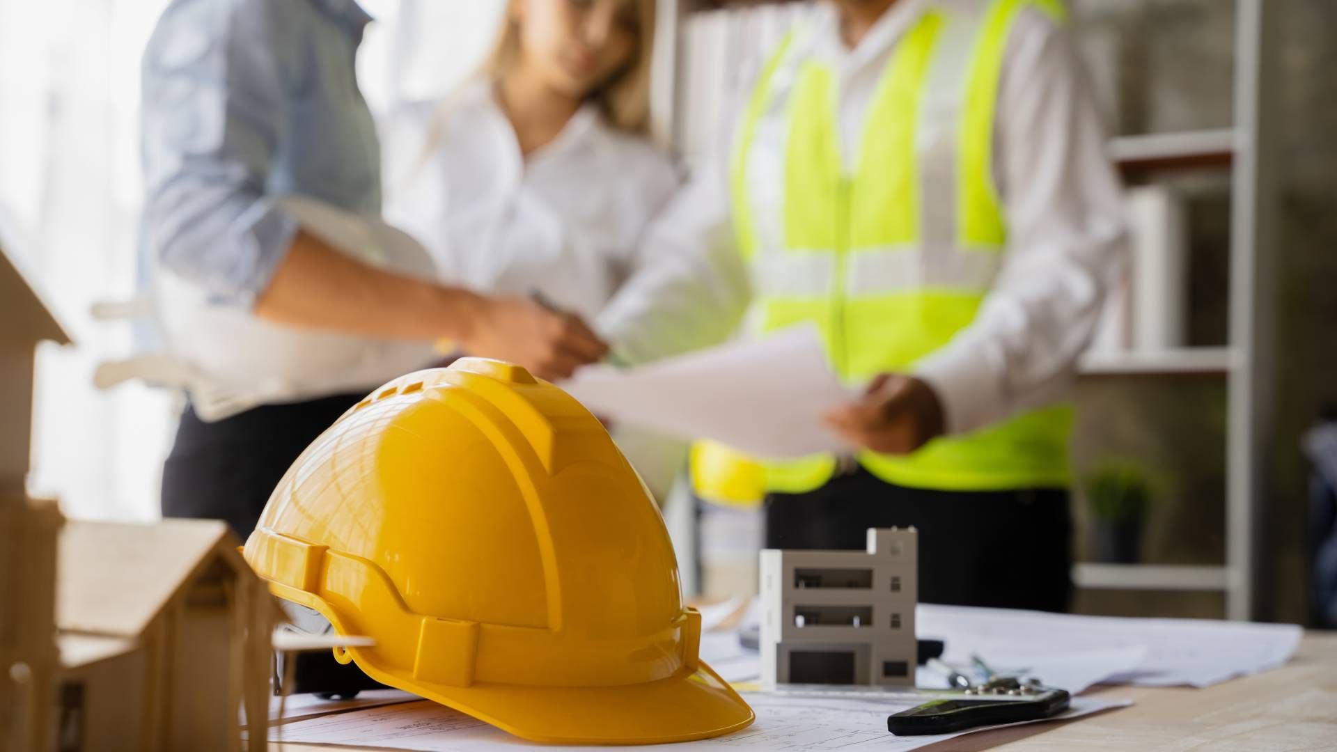 A yellow hard hat is sitting on a table next to a group of construction workers.