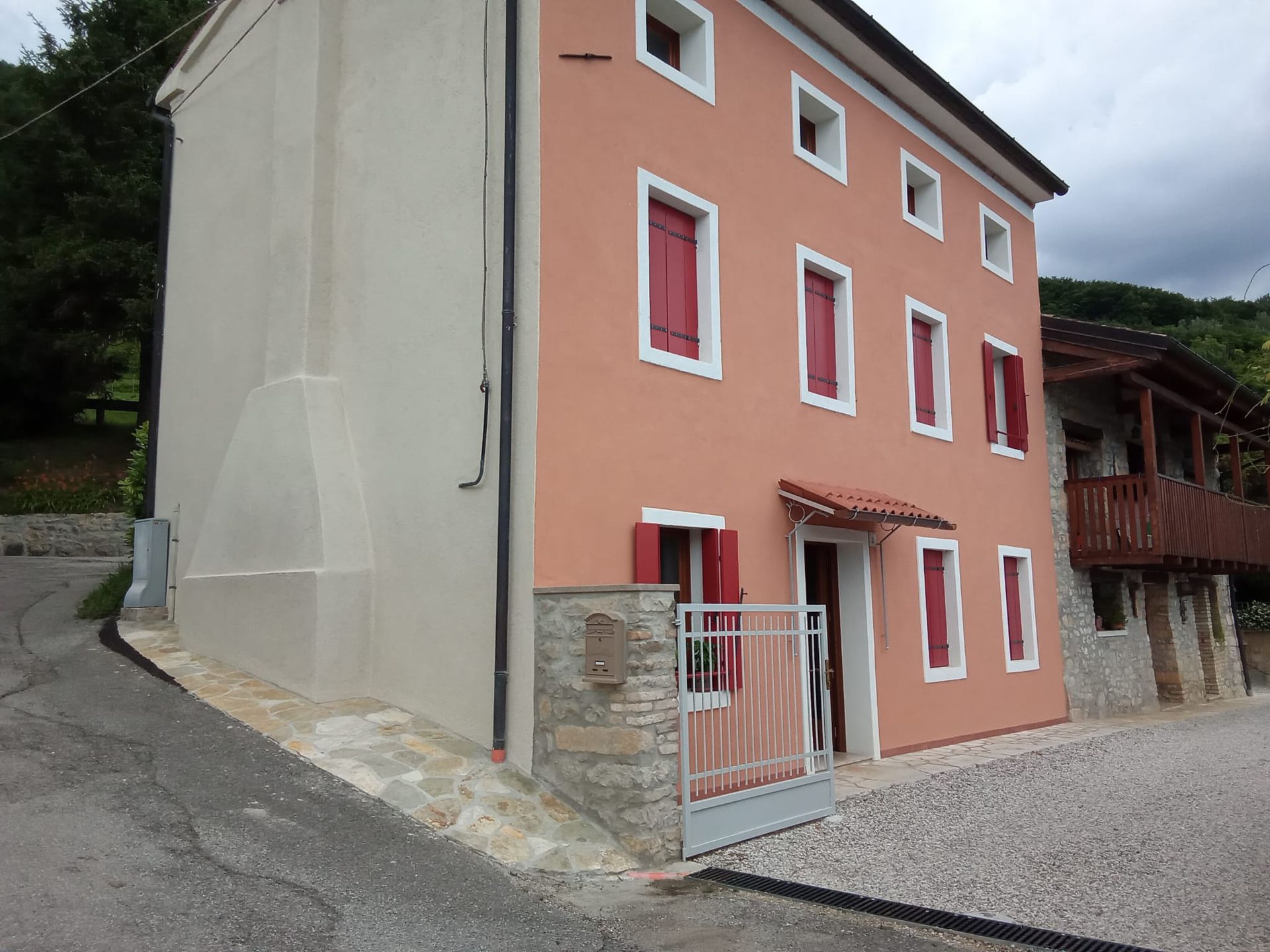 Casa rosa e bianca accanto a una strada sterrata, con un cancello e cielo nuvoloso.