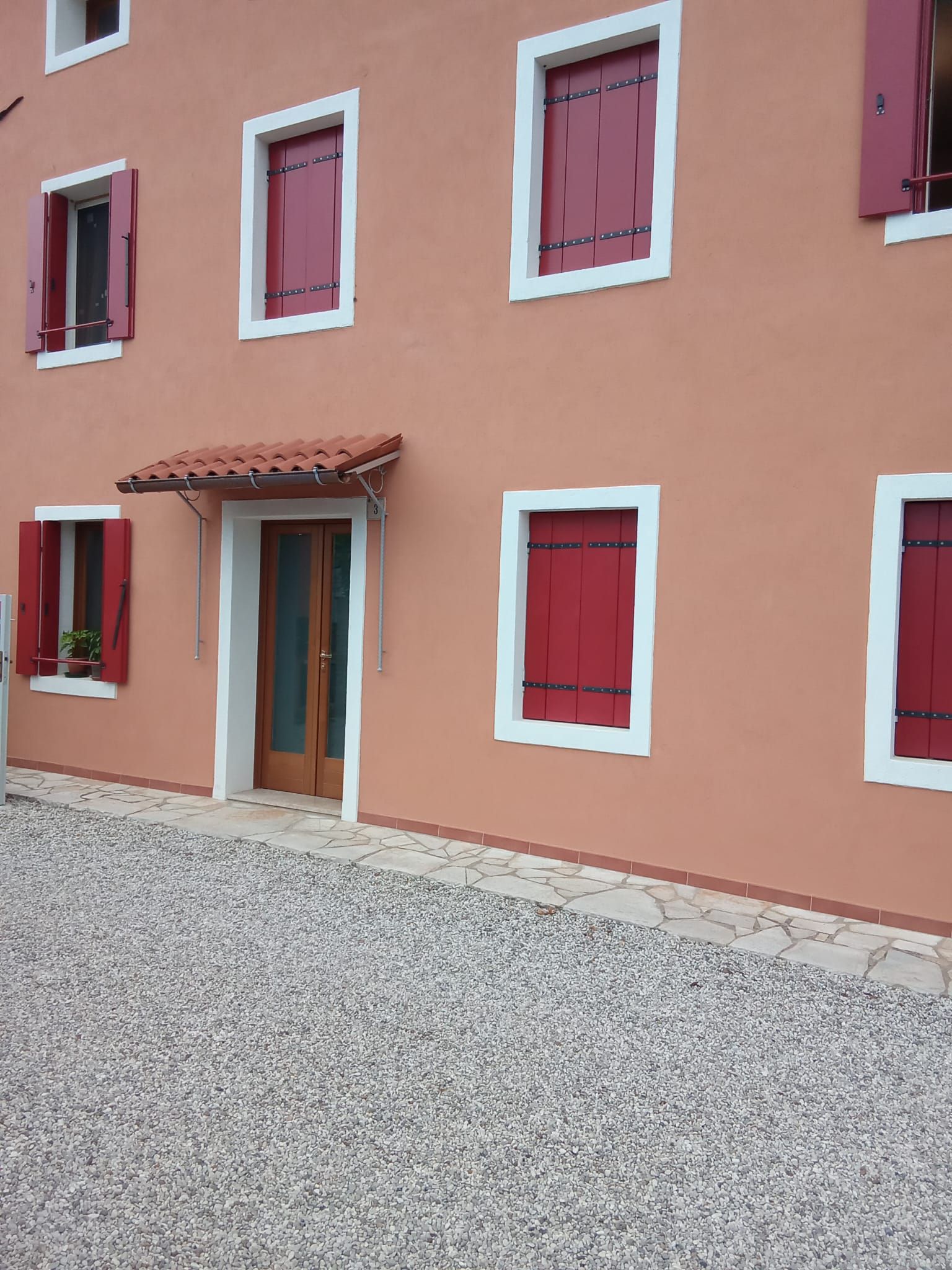 Facciata della casa in stucco rosa con finestre con cornici bianche e un piccolo ingresso piastrellato su ghiaia