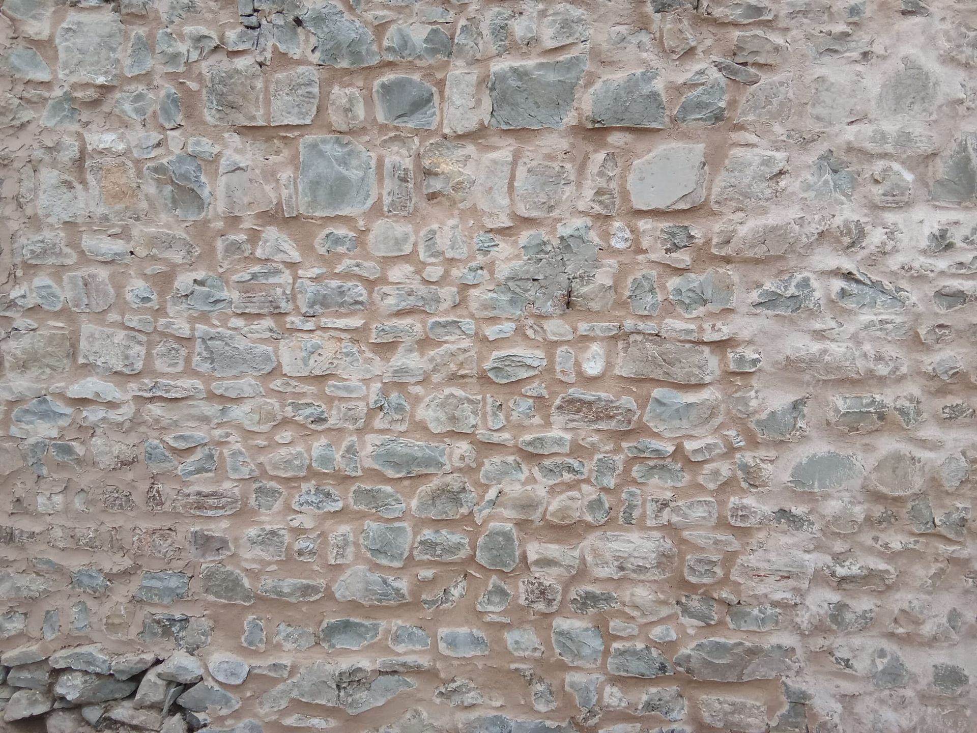 Primo piano di un muro di pietra consumato dal tempo, con pietre grezze di colore beige e grigio e malta.