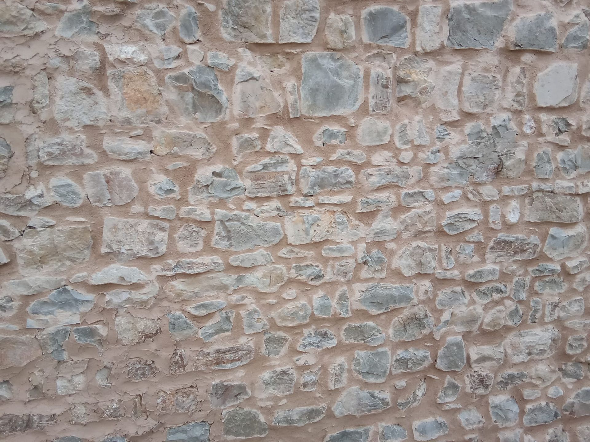 Primo piano di un muro di pietra beige grezza con rocce irregolari e malta