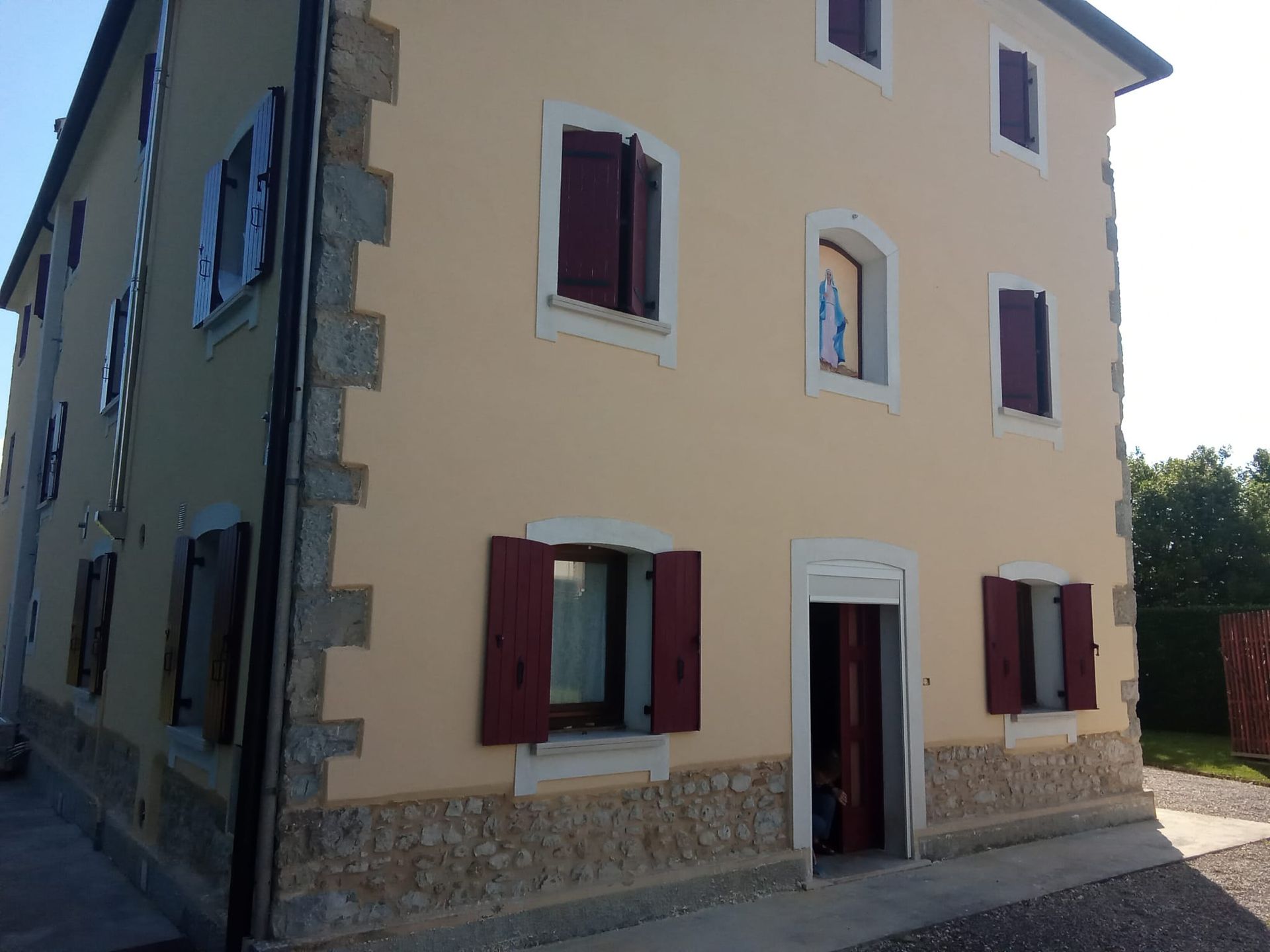 Casa beige a tre piani con persiane rosse e basamento in pietra, situata in una strada tranquilla.