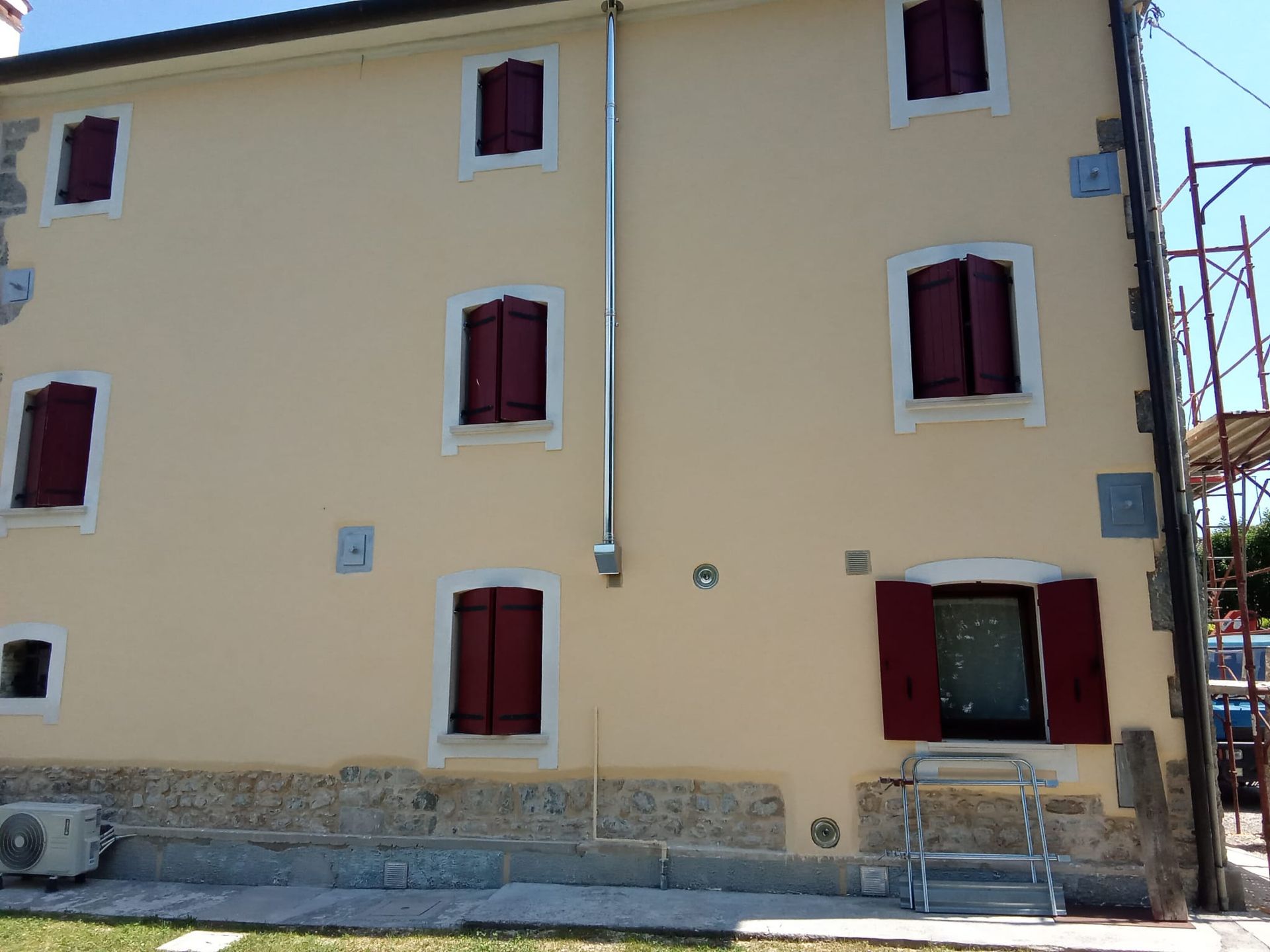 Edificio color crema con finestre dalle persiane rosse e portone d'ingresso centrale, affacciato su una strada soleggiata.