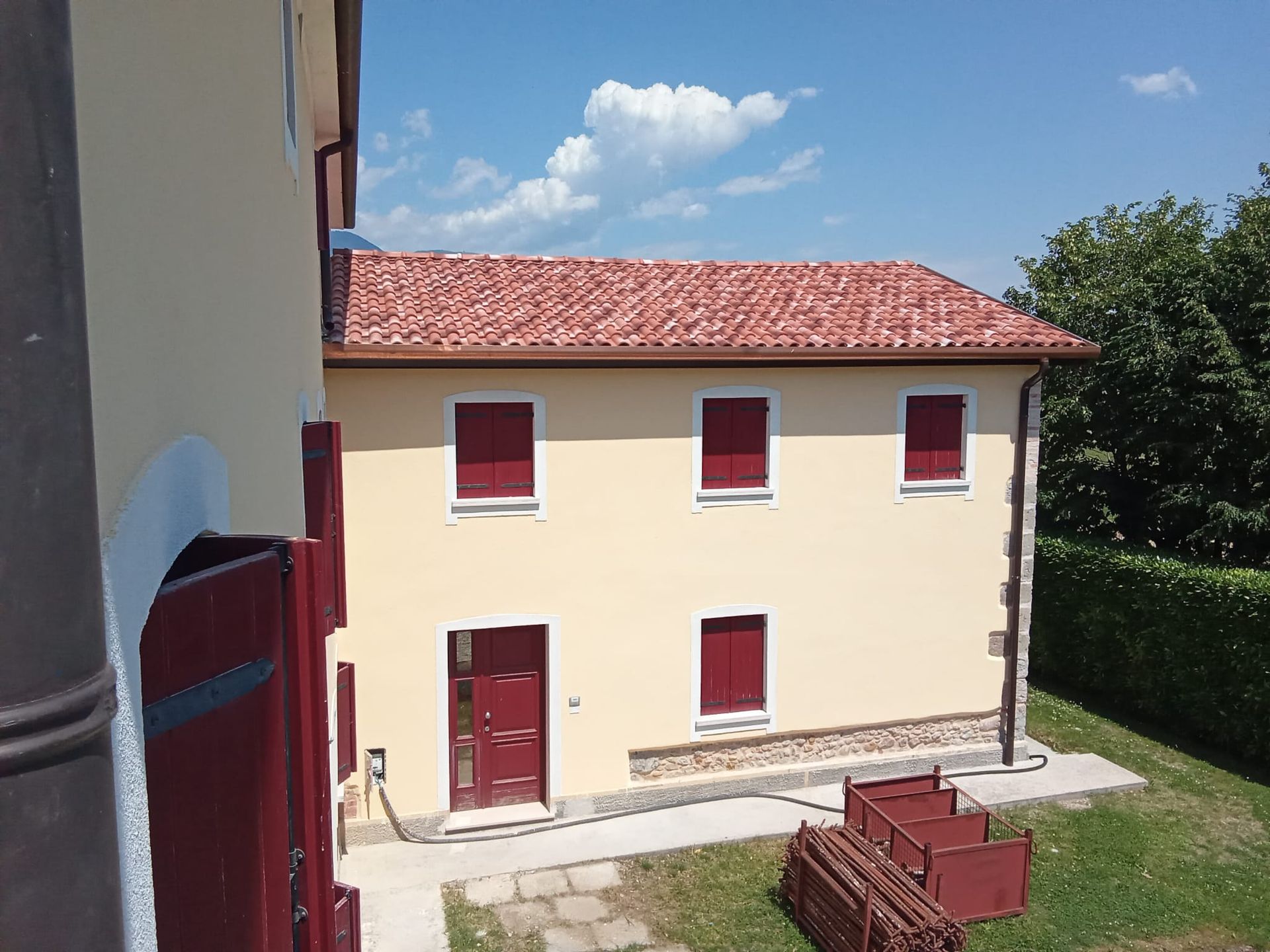 Casa a due piani color crema con persiane e tetto rossi, vista da un cortile erboso in una giornata di sole.