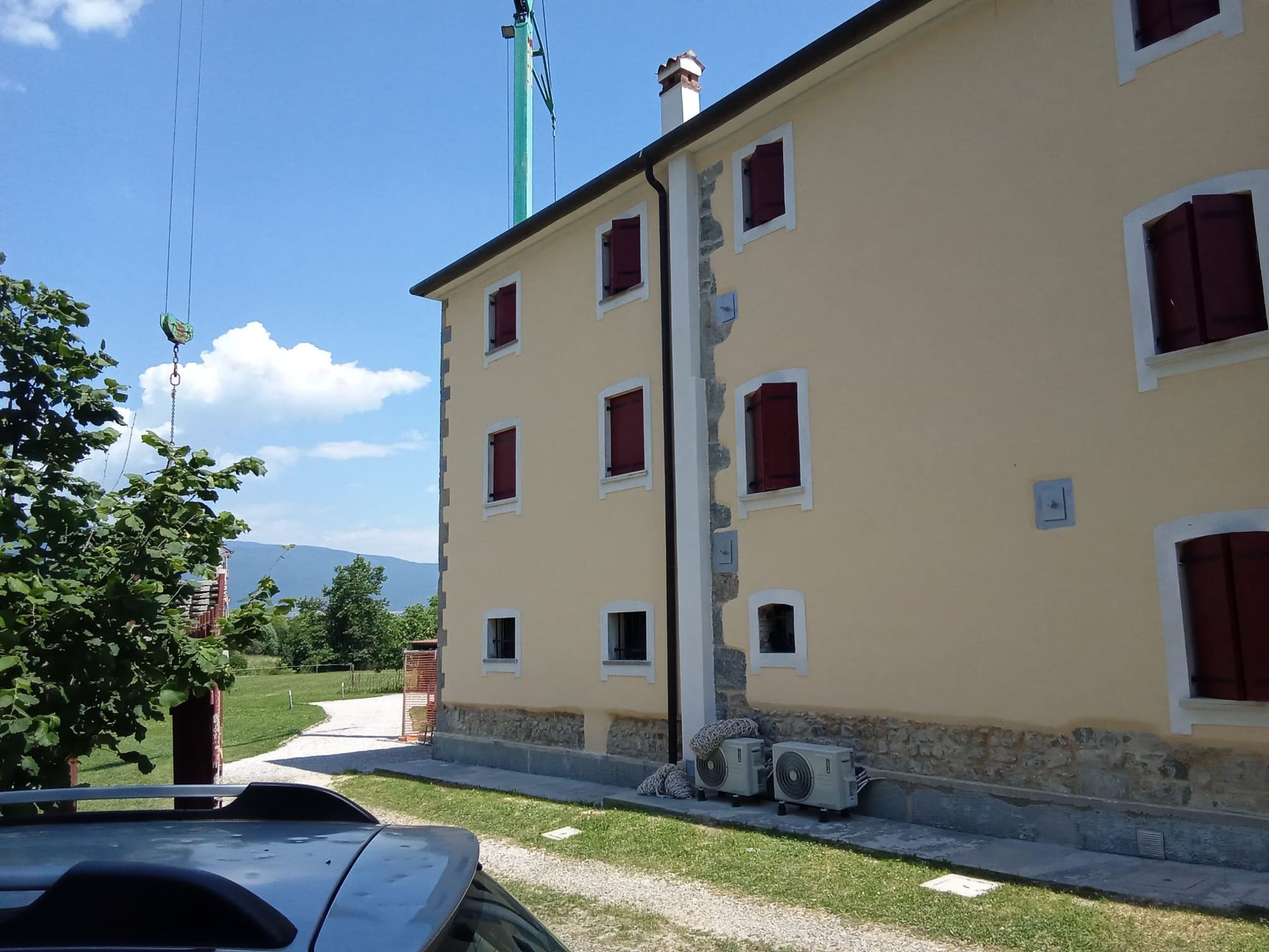 Casa gialla con persiane rosse accanto a un vialetto di ghiaia e vista sulle montagne sotto un cielo azzurro.