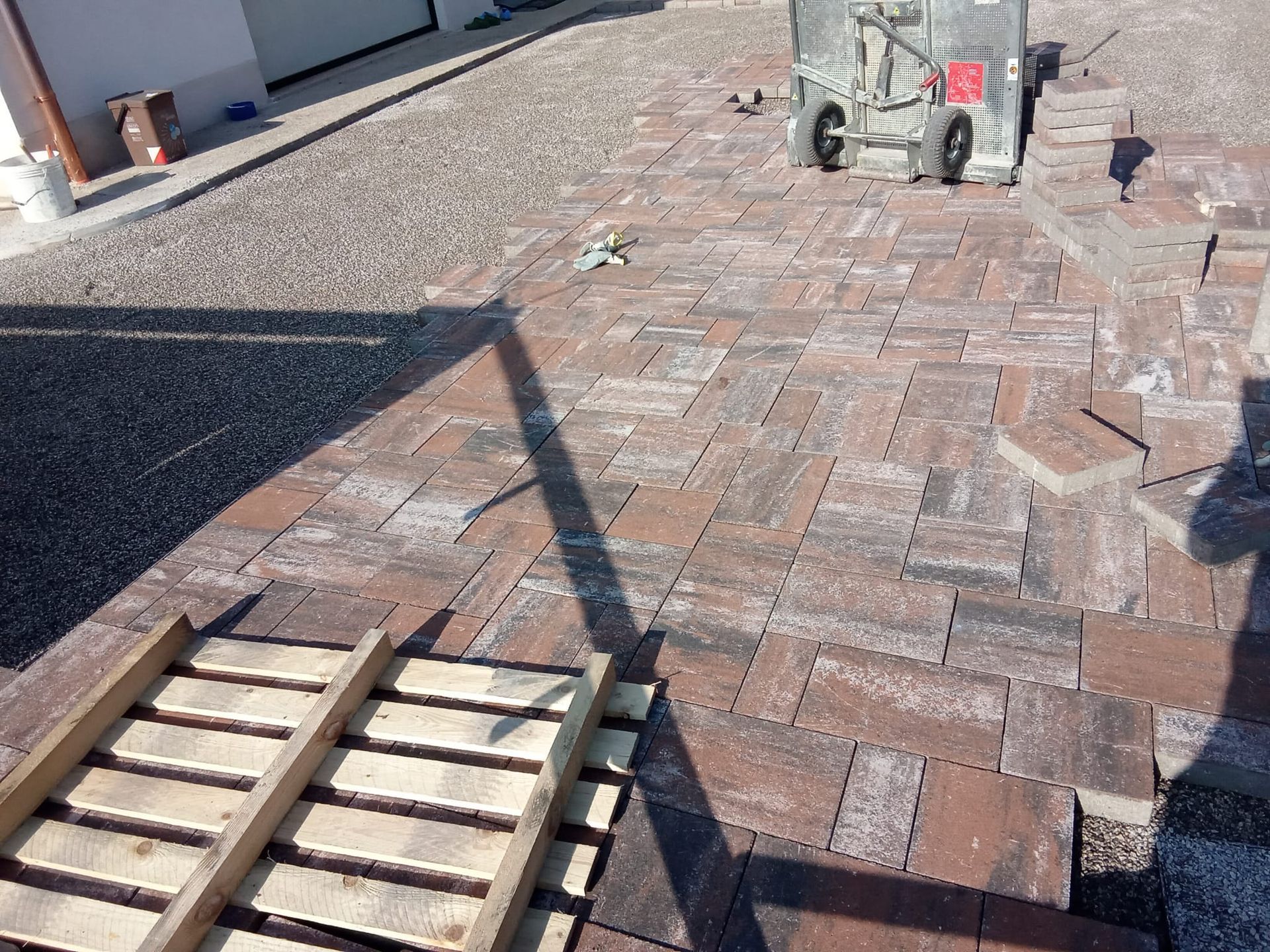 Passaggio pedonale lastricato in mattoni accanto a un edificio, con pallet impilati e attrezzature edili sullo sfondo.