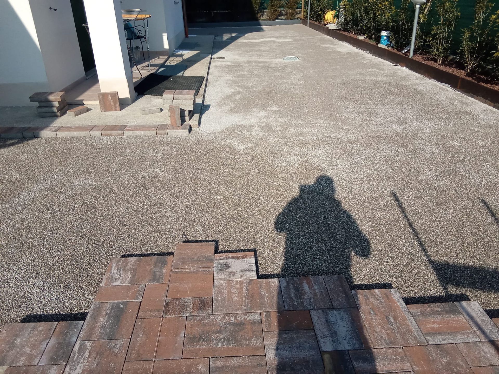 Vialetto d'ingresso con scalini in mattoni che conducono a un vialetto di ghiaia accanto a una casa, con l'ombra di una persona in primo piano.