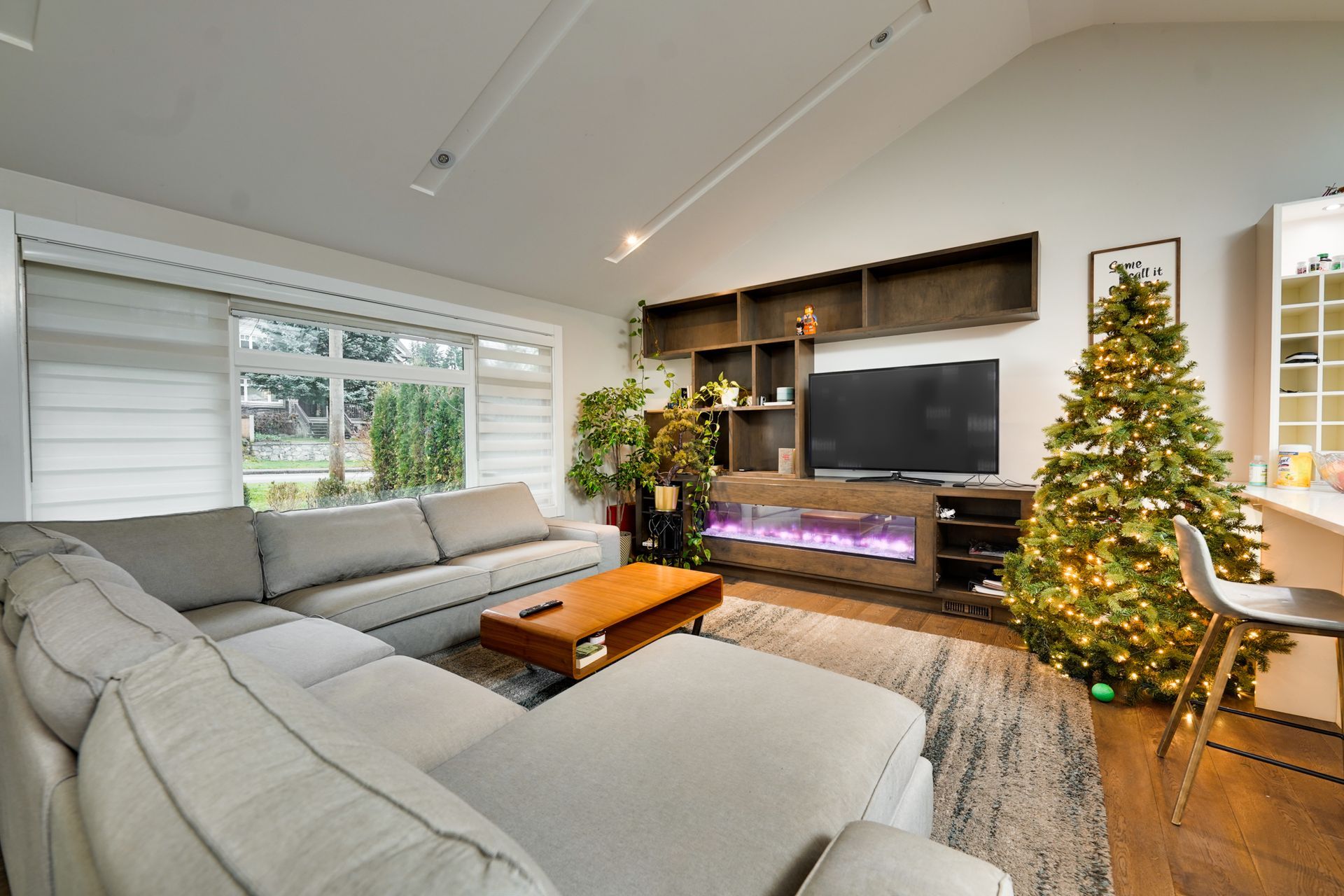 Cozy living room with gray sectional sofa, TV, Christmas tree, and wooden entertainment center.