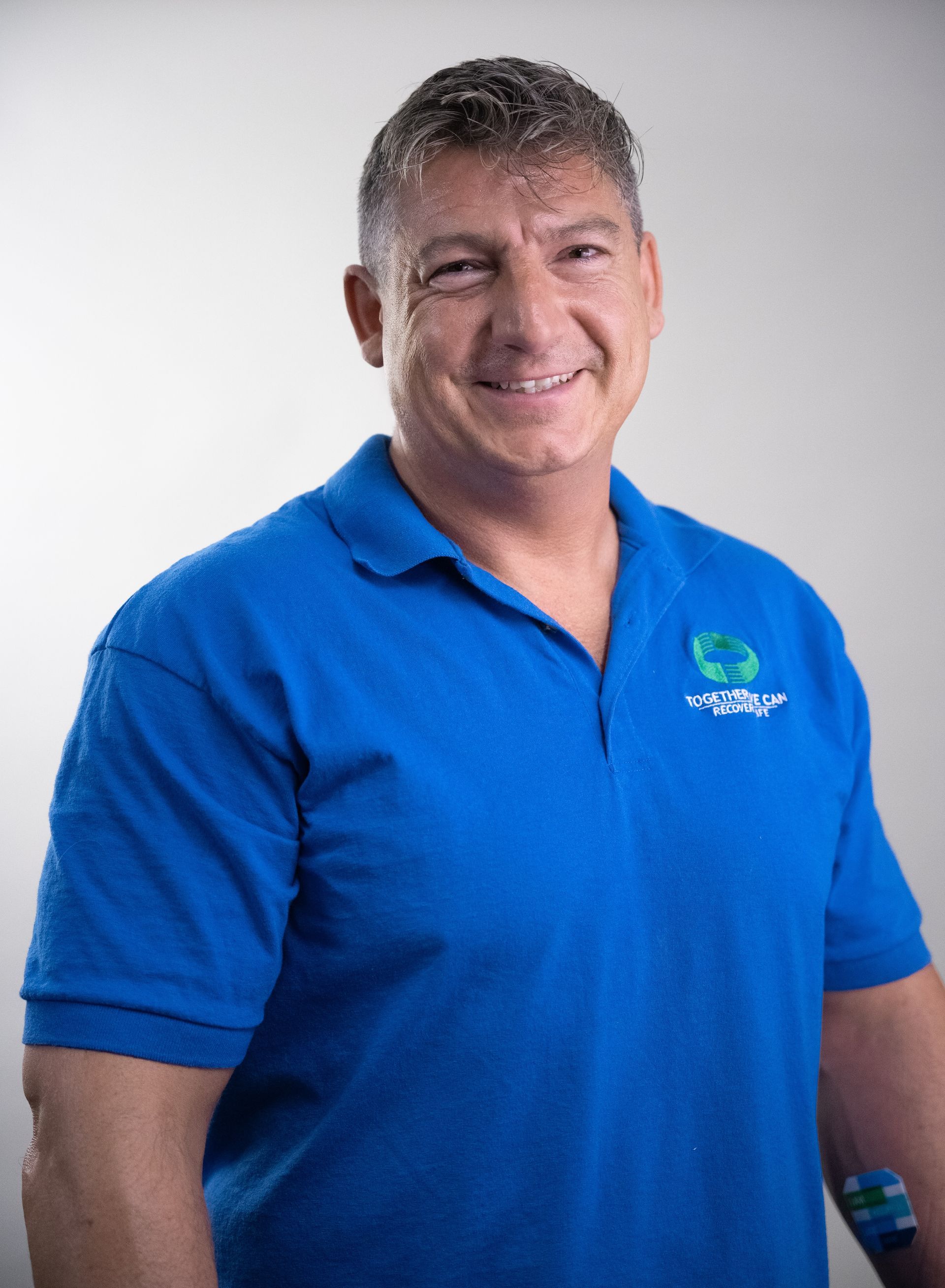 Man in blue polo shirt smiling, looking at the camera; white background.