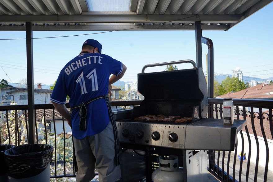 Man in Bichette jersey grilling outside on a deck, overlooking city and mountains.