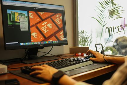 Person using a keyboard and mouse at a desktop computer showing a colorful design on screen