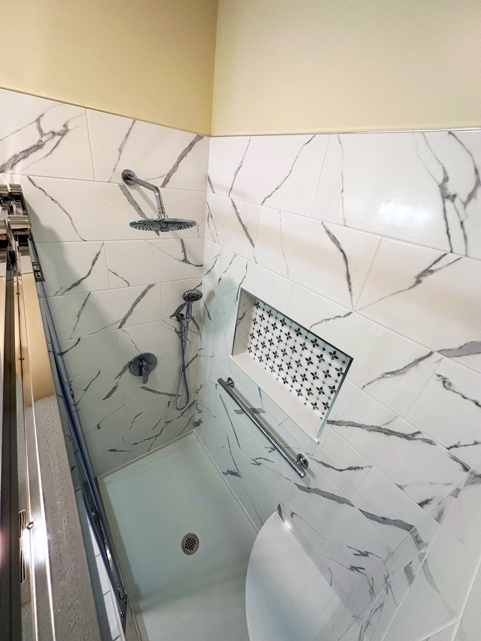 White marble shower with chrome fixtures, a built-in shelf, and a glass shower door.