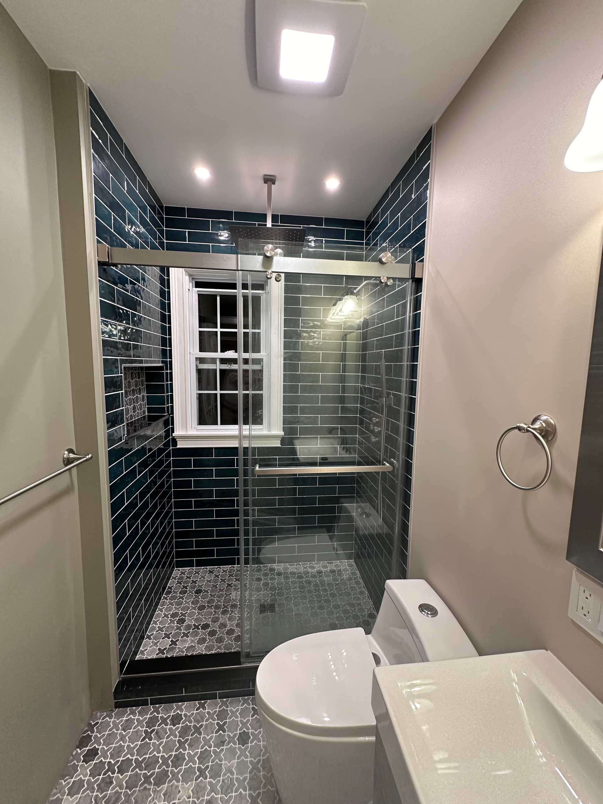 Small bathroom with dark blue tiled shower, glass door, and toilet.
