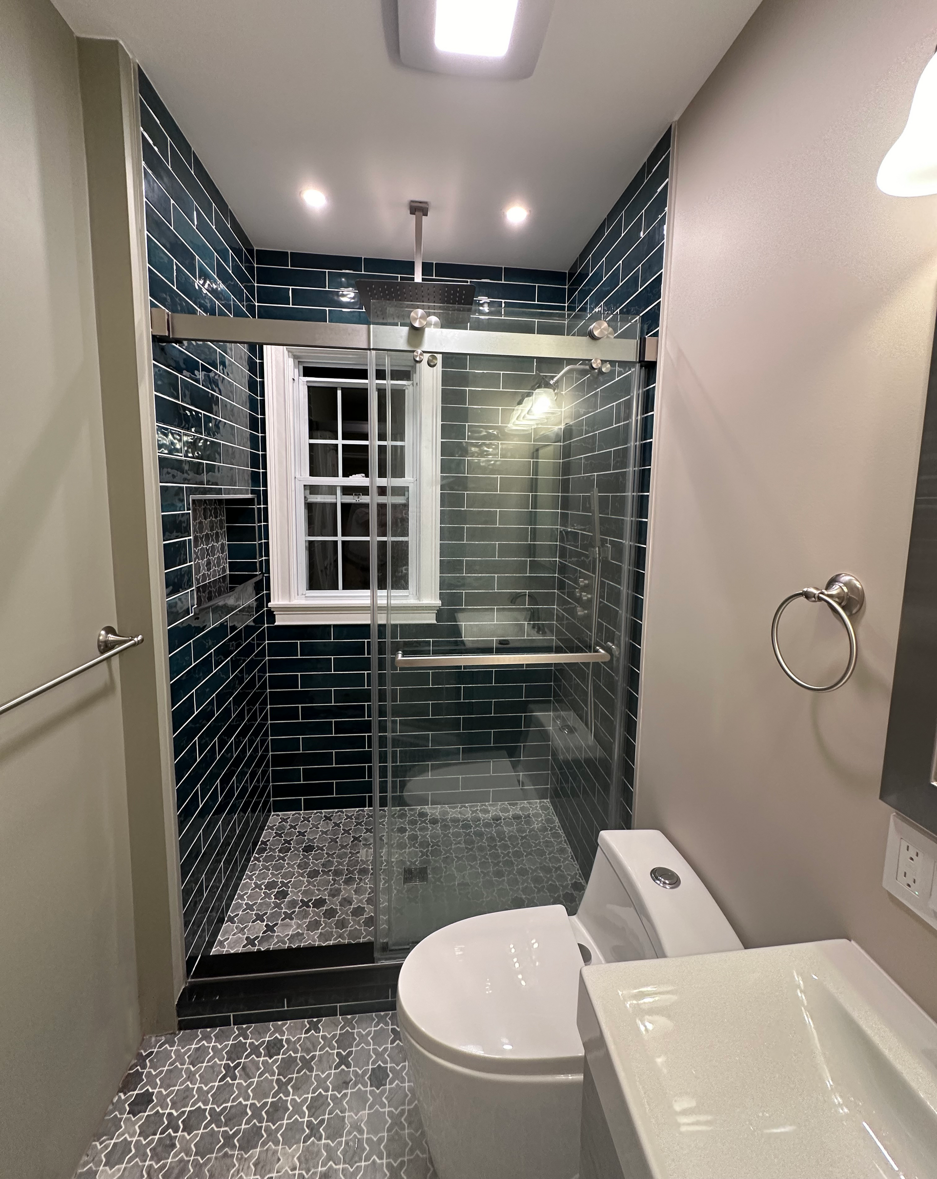 Bathroom with a glass shower, dark blue tiled walls, and a white toilet.