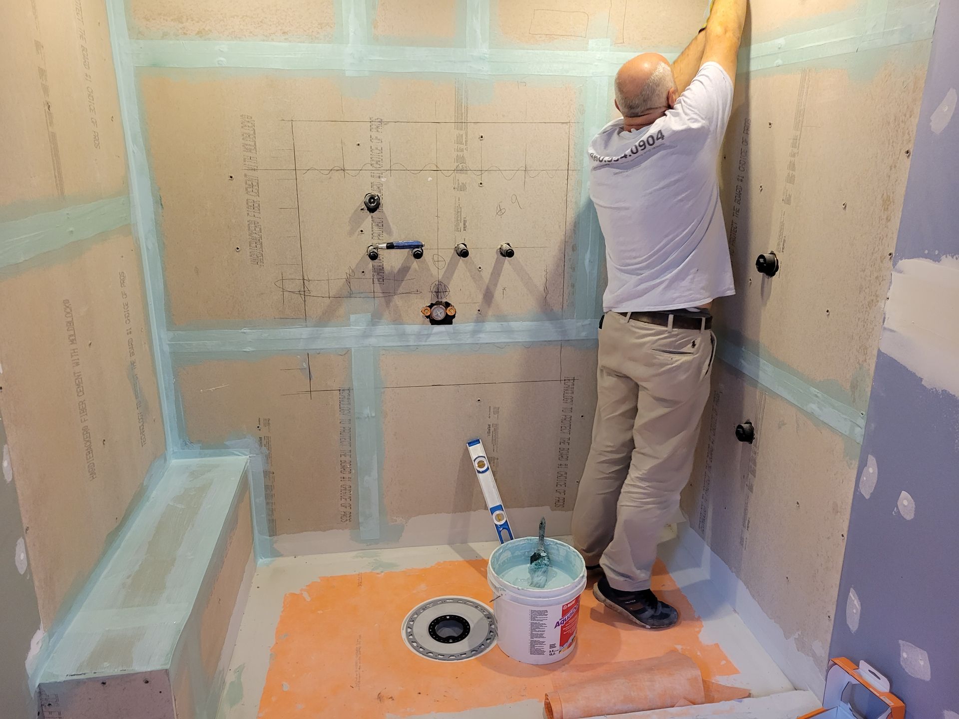 A man is standing in a bathroom with a bucket of paint.