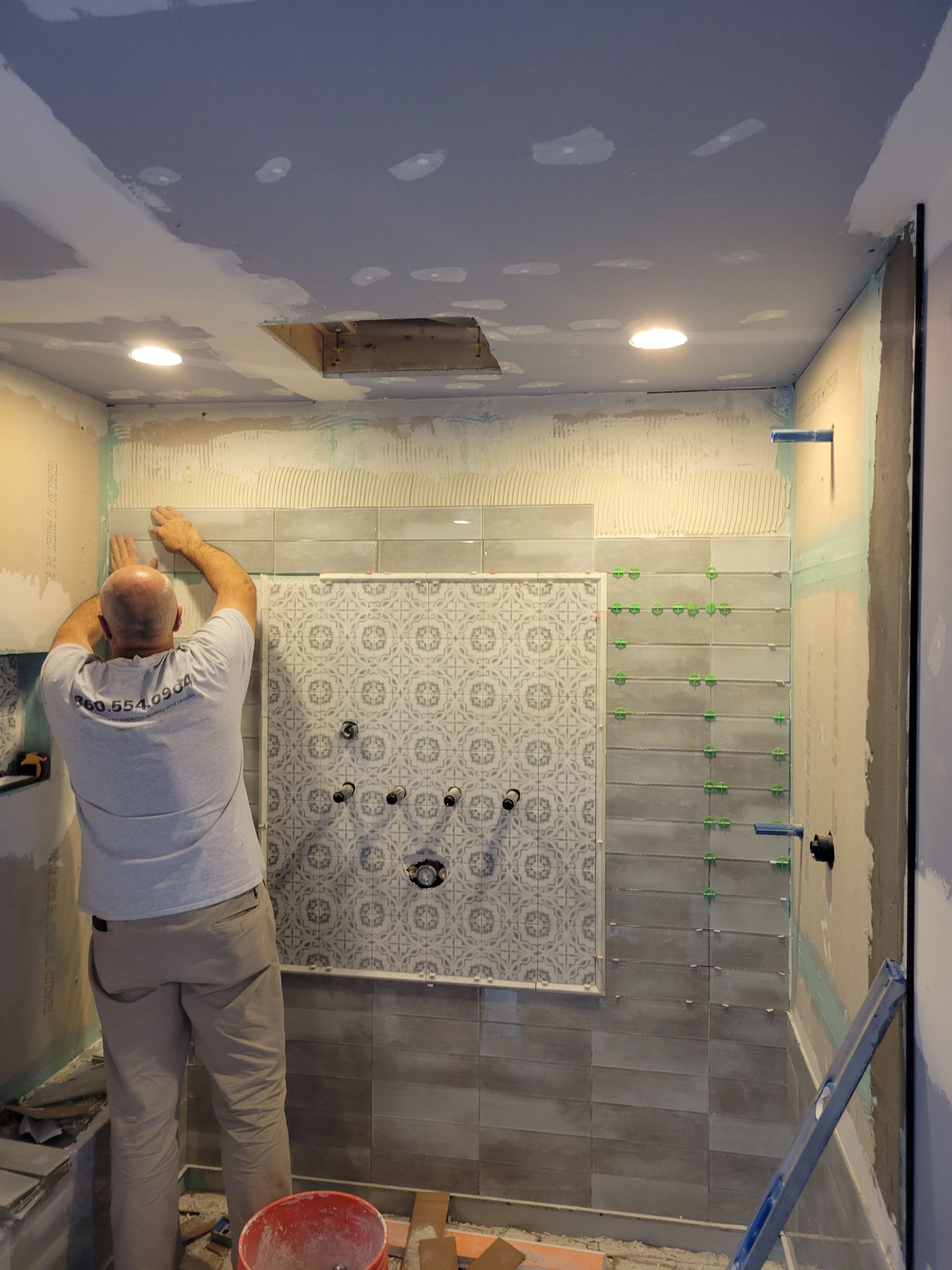 A man is installing tiles on a wall in a bathroom.