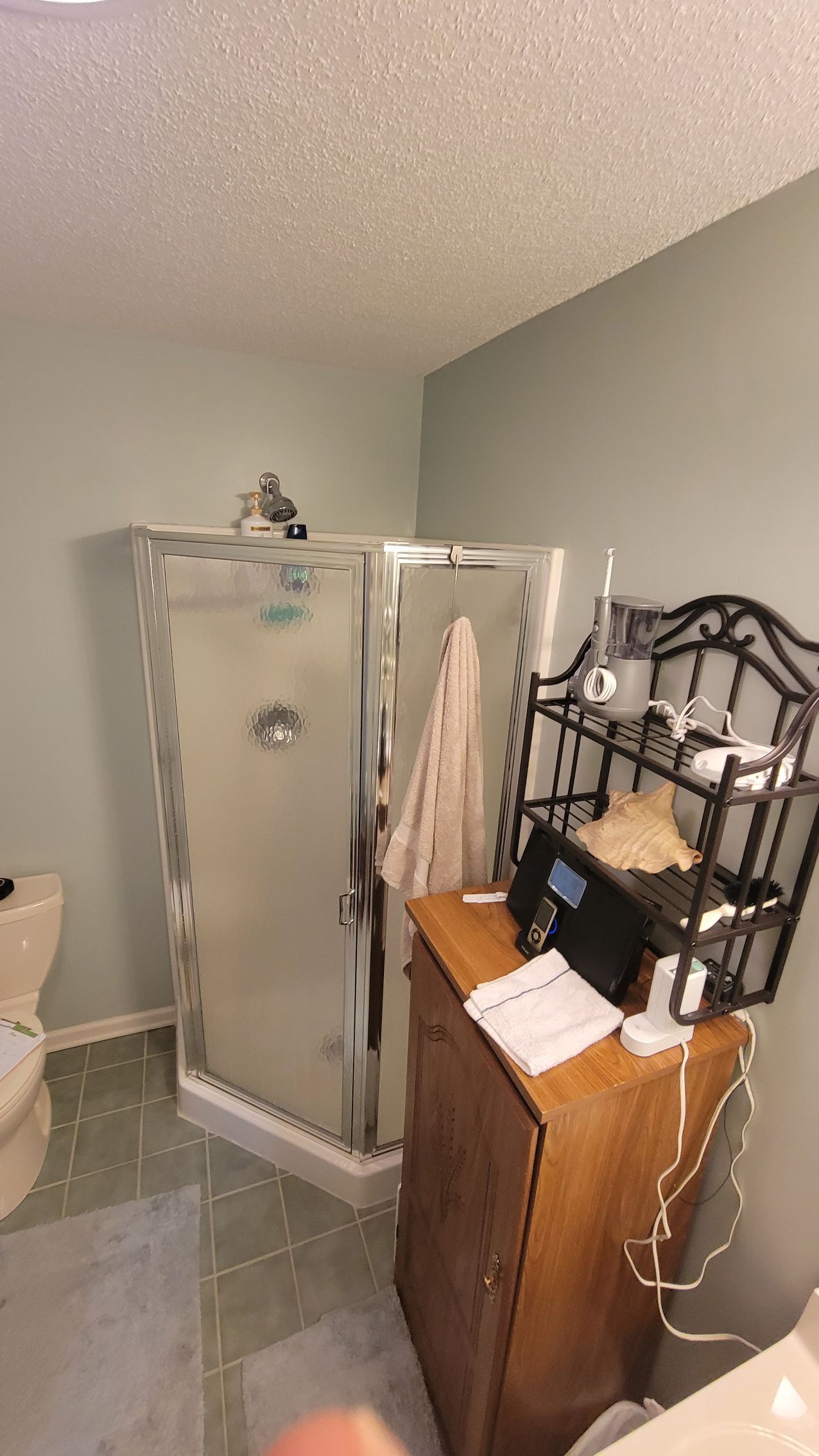 A bathroom with a toilet , sink , shower and dresser.
