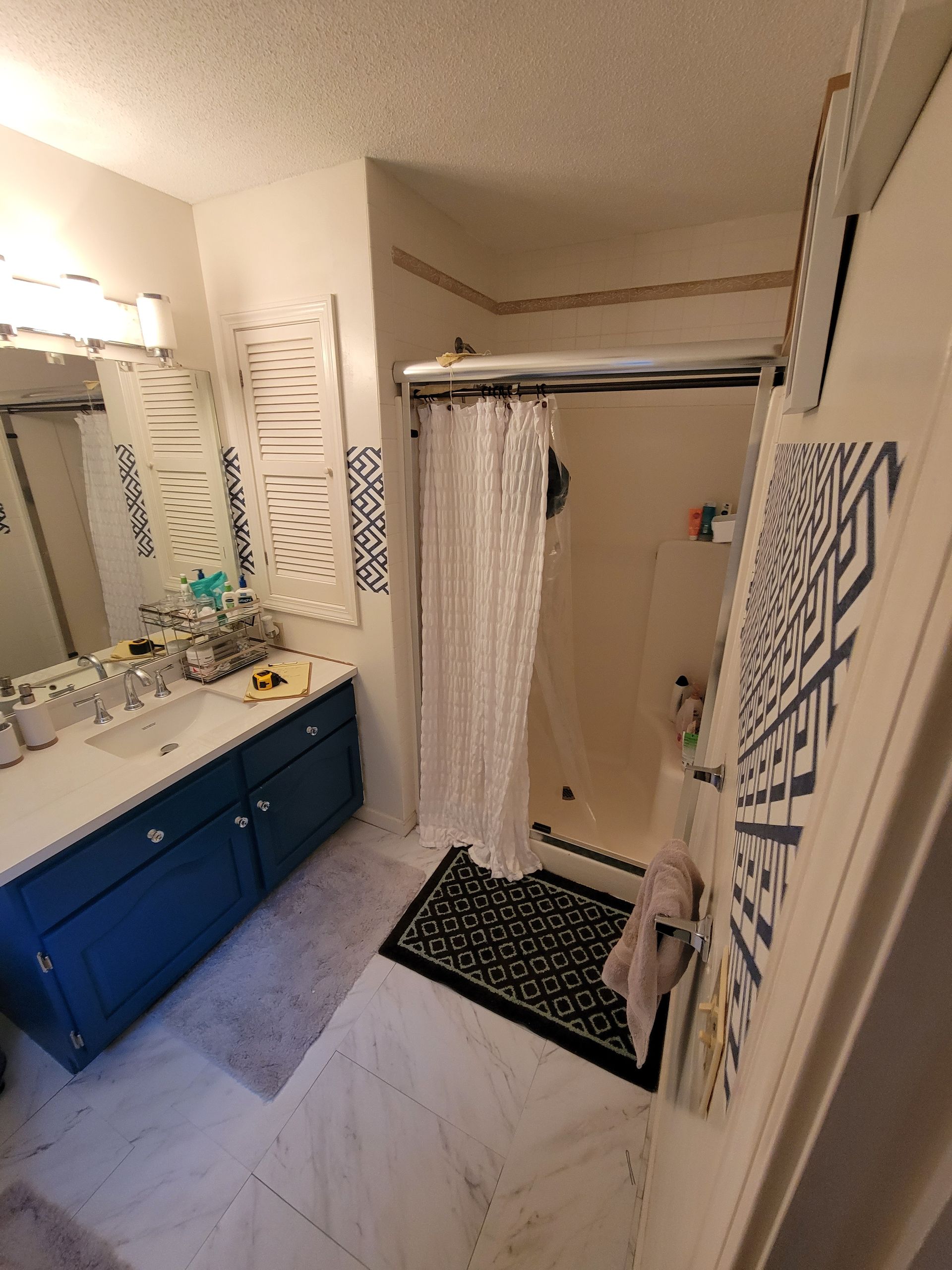 A bathroom with a shower , sink , mirror and blue cabinets.