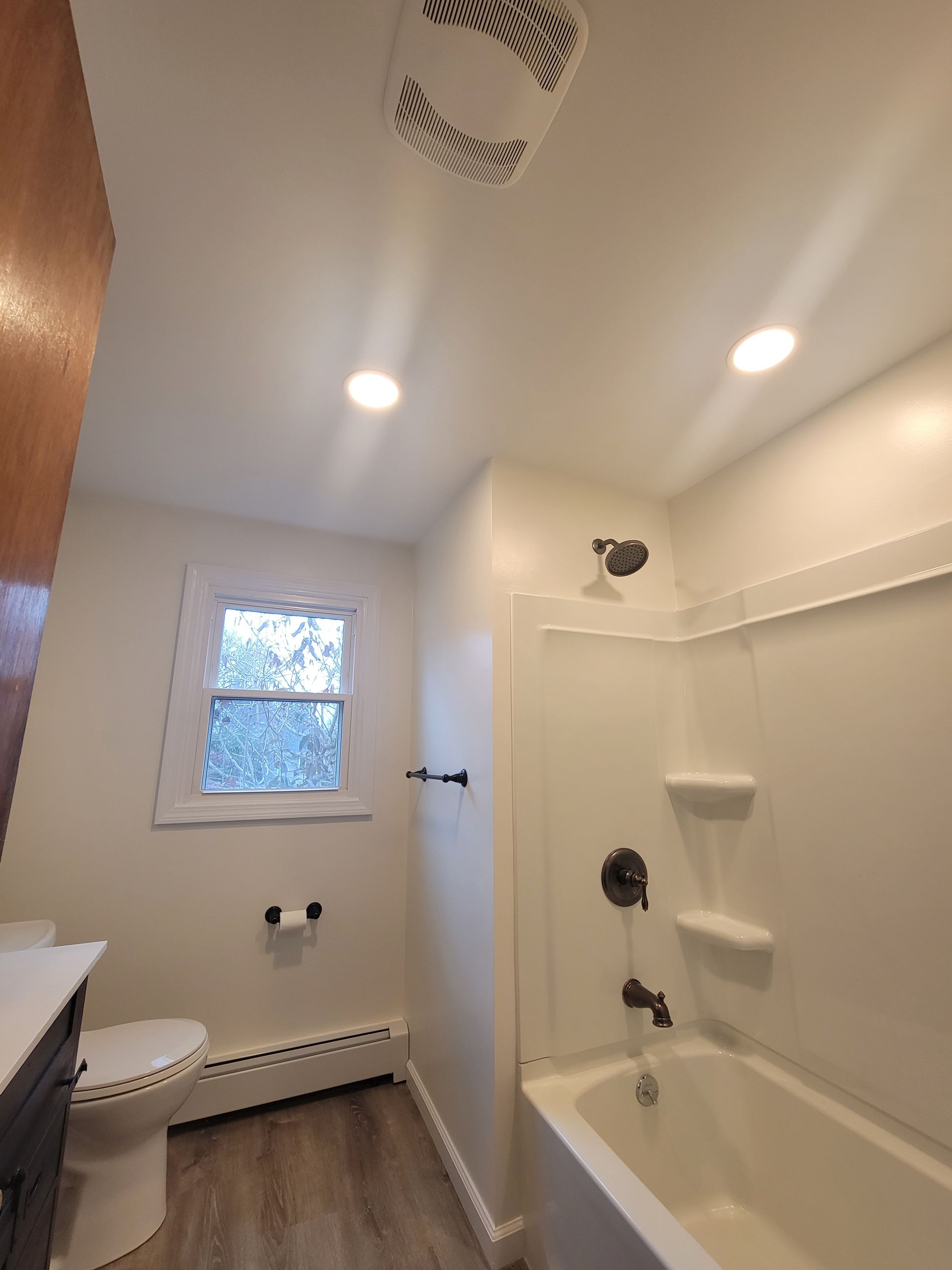 Bathroom with white walls, tub, toilet, showerhead, and small window.