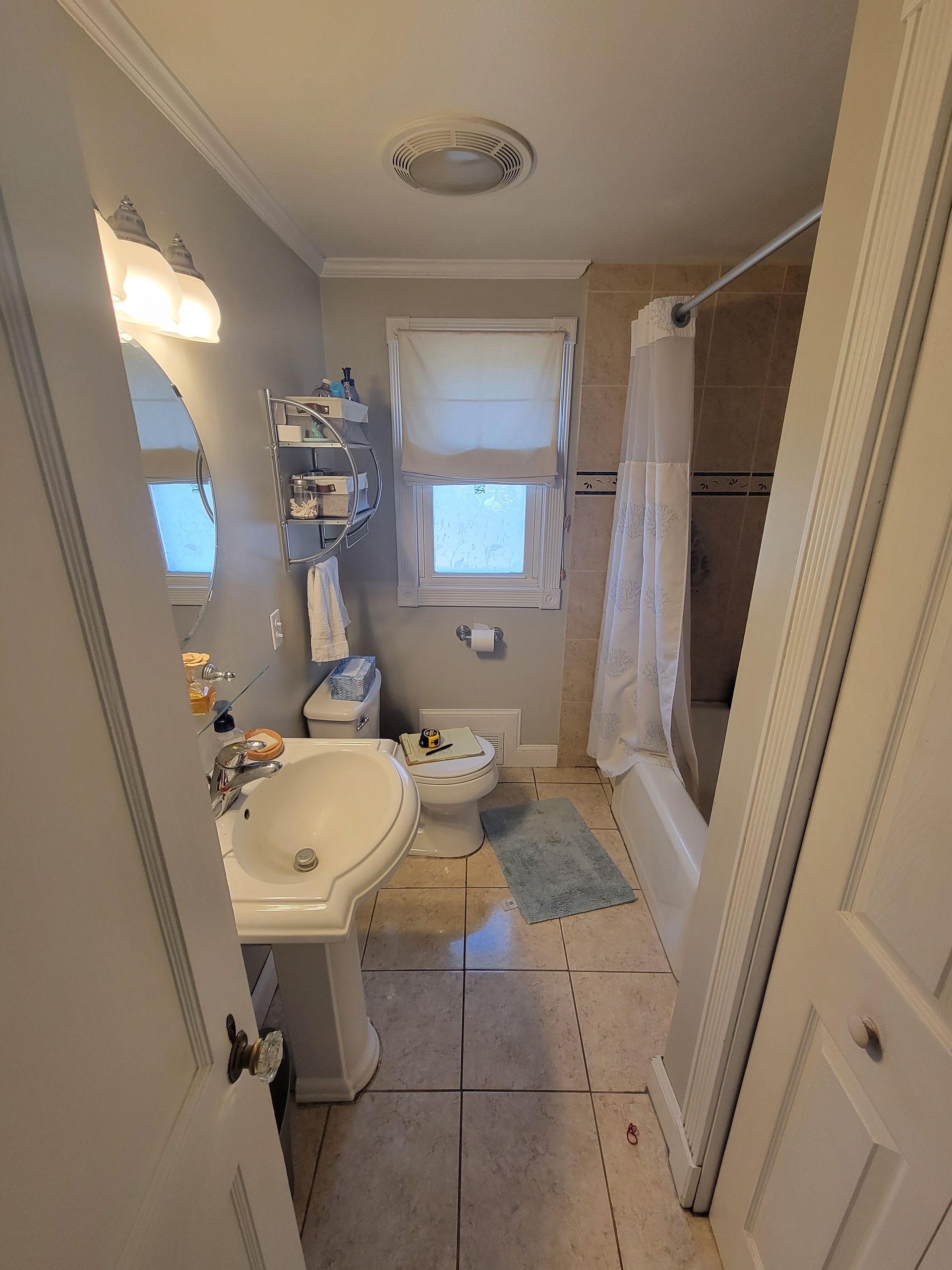 A bathroom with a sink , toilet , shower and window.