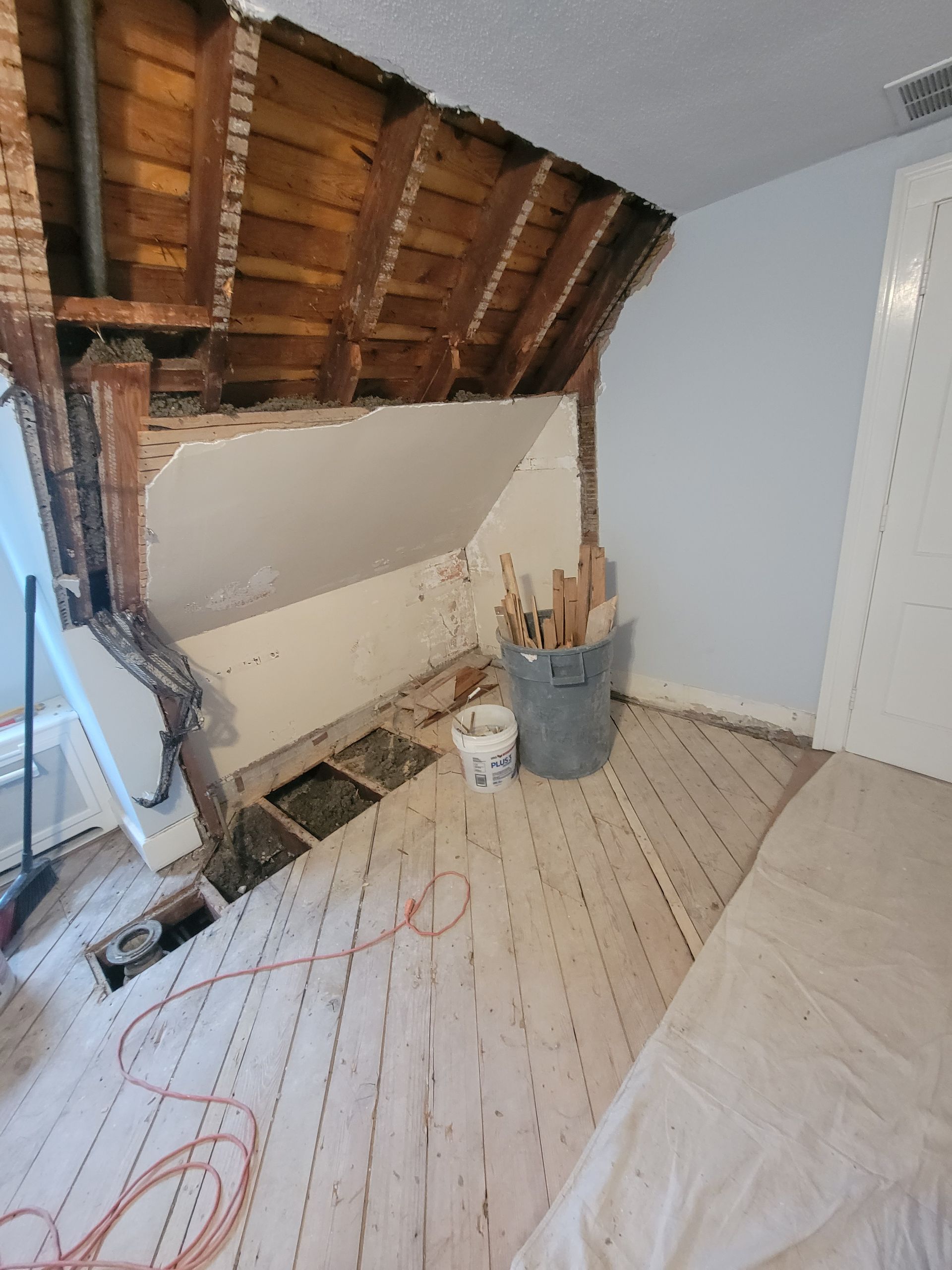 A room with a hole in the ceiling and a bucket of tools on the floor.