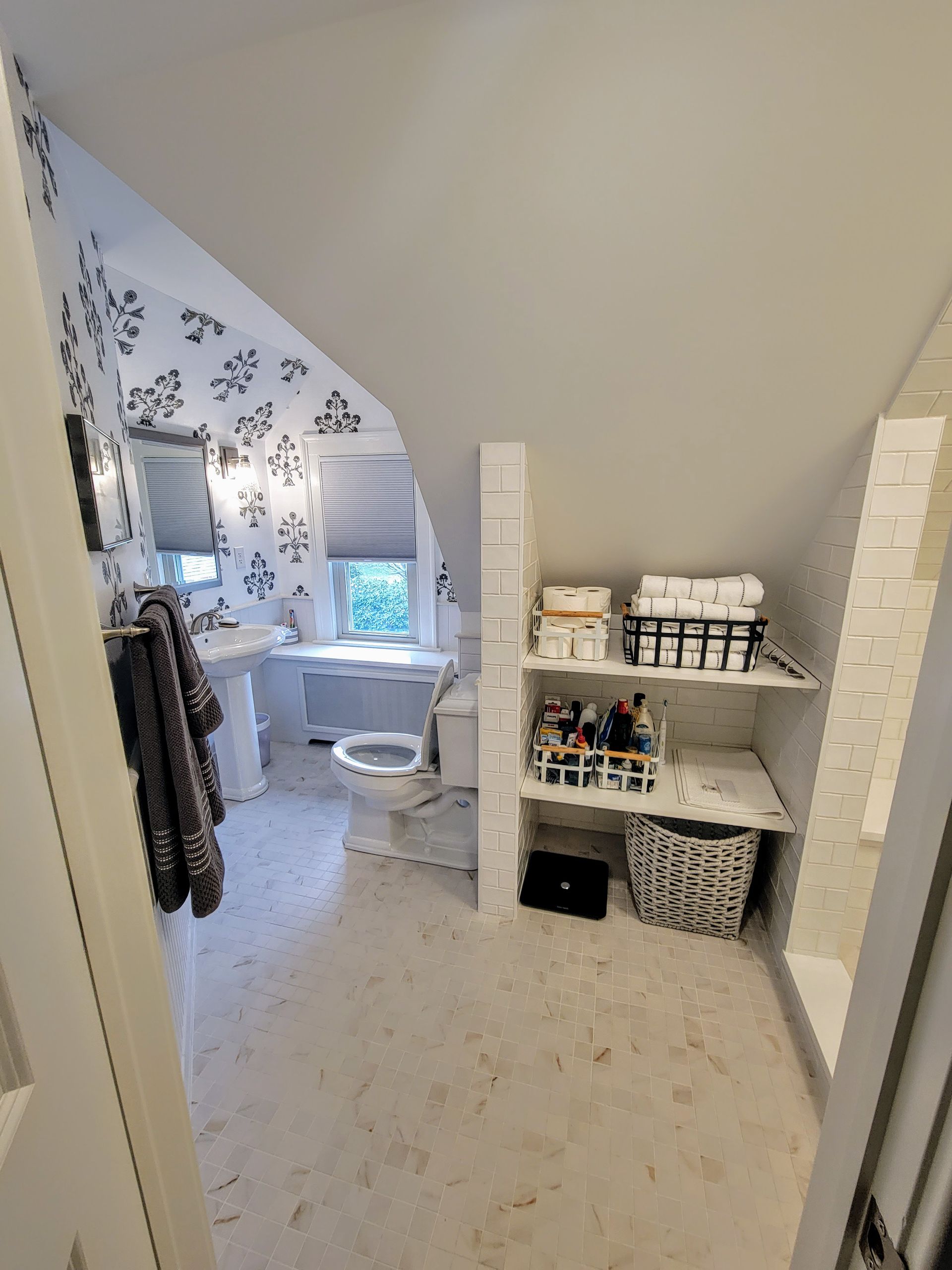 A bathroom with a toilet , sink , and shelves.