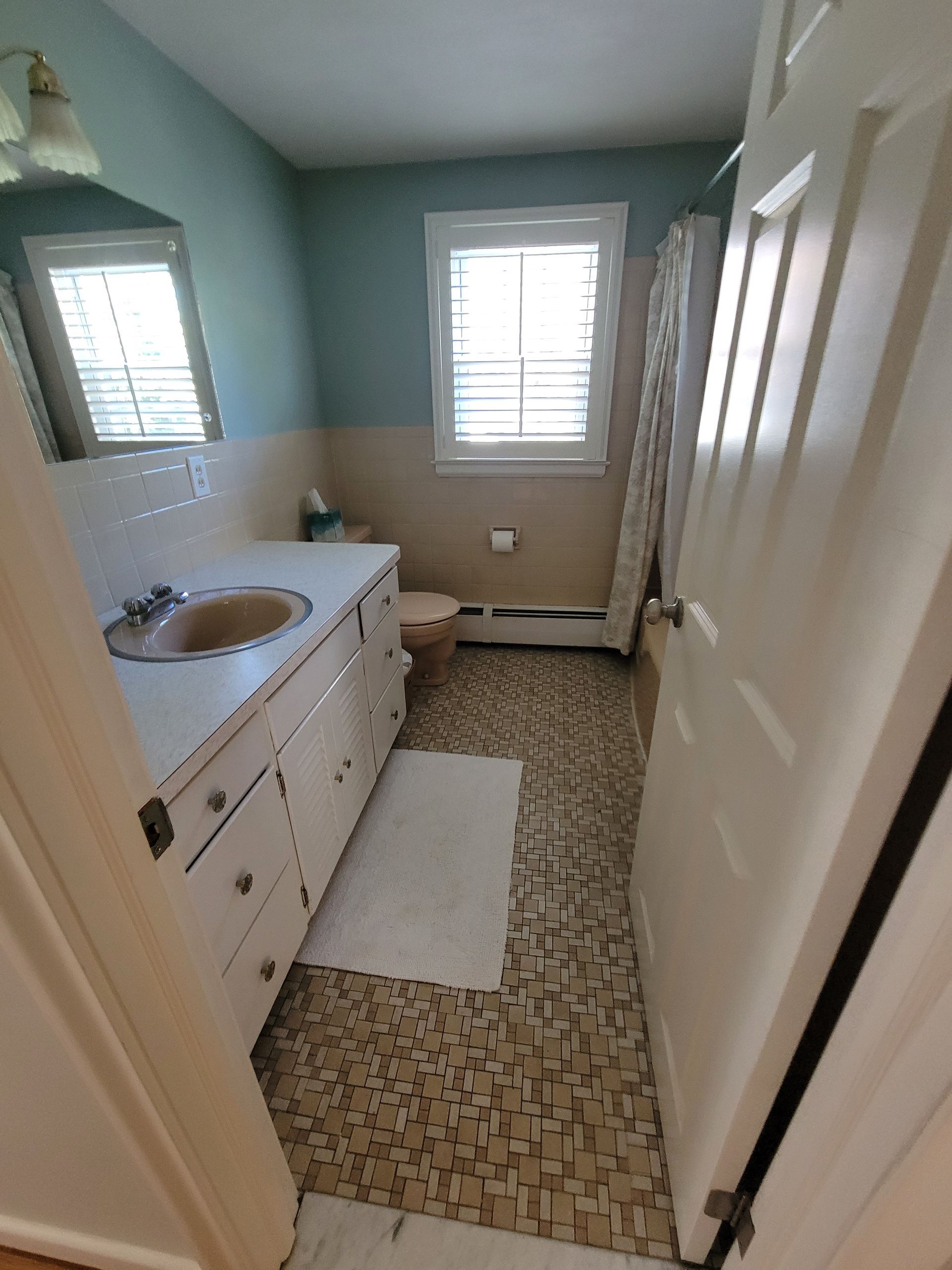 A bathroom with a sink , toilet , mirror and window.