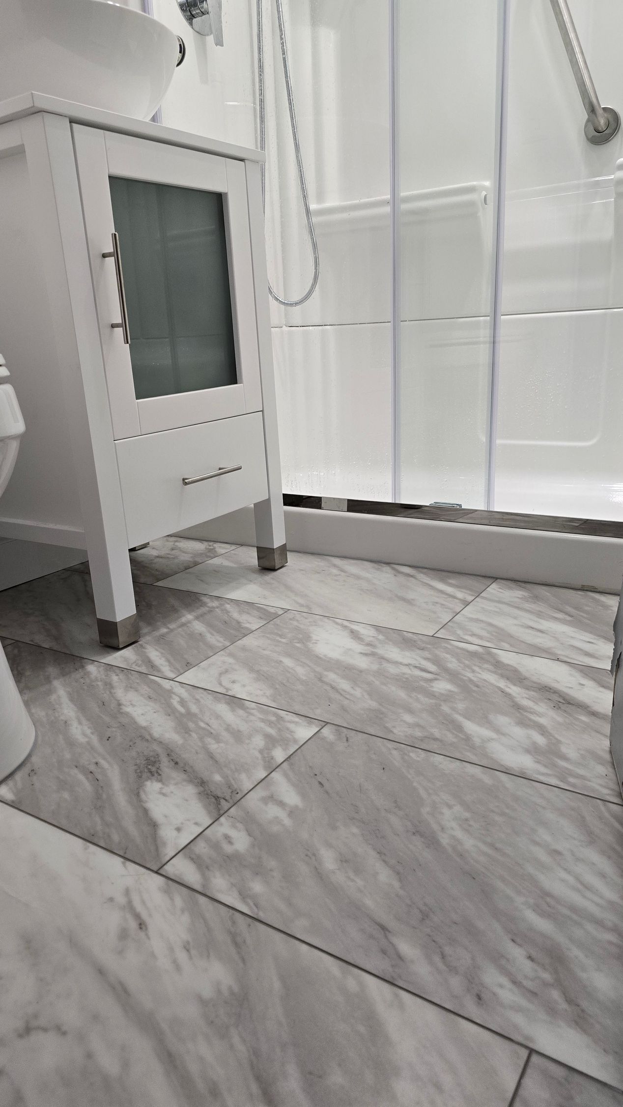 White bathroom with marble tile floor, vanity, and glass shower enclosure.