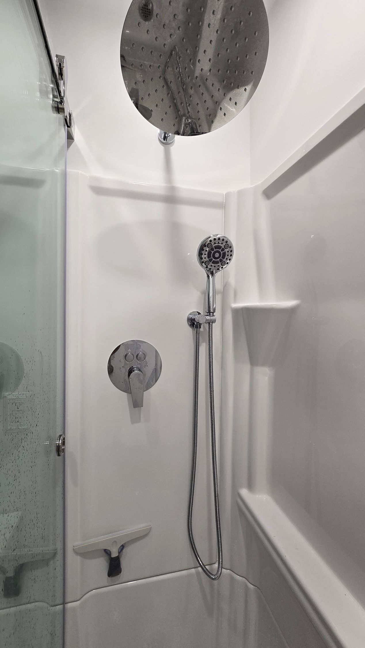 White shower stall with glass door and silver fixtures.